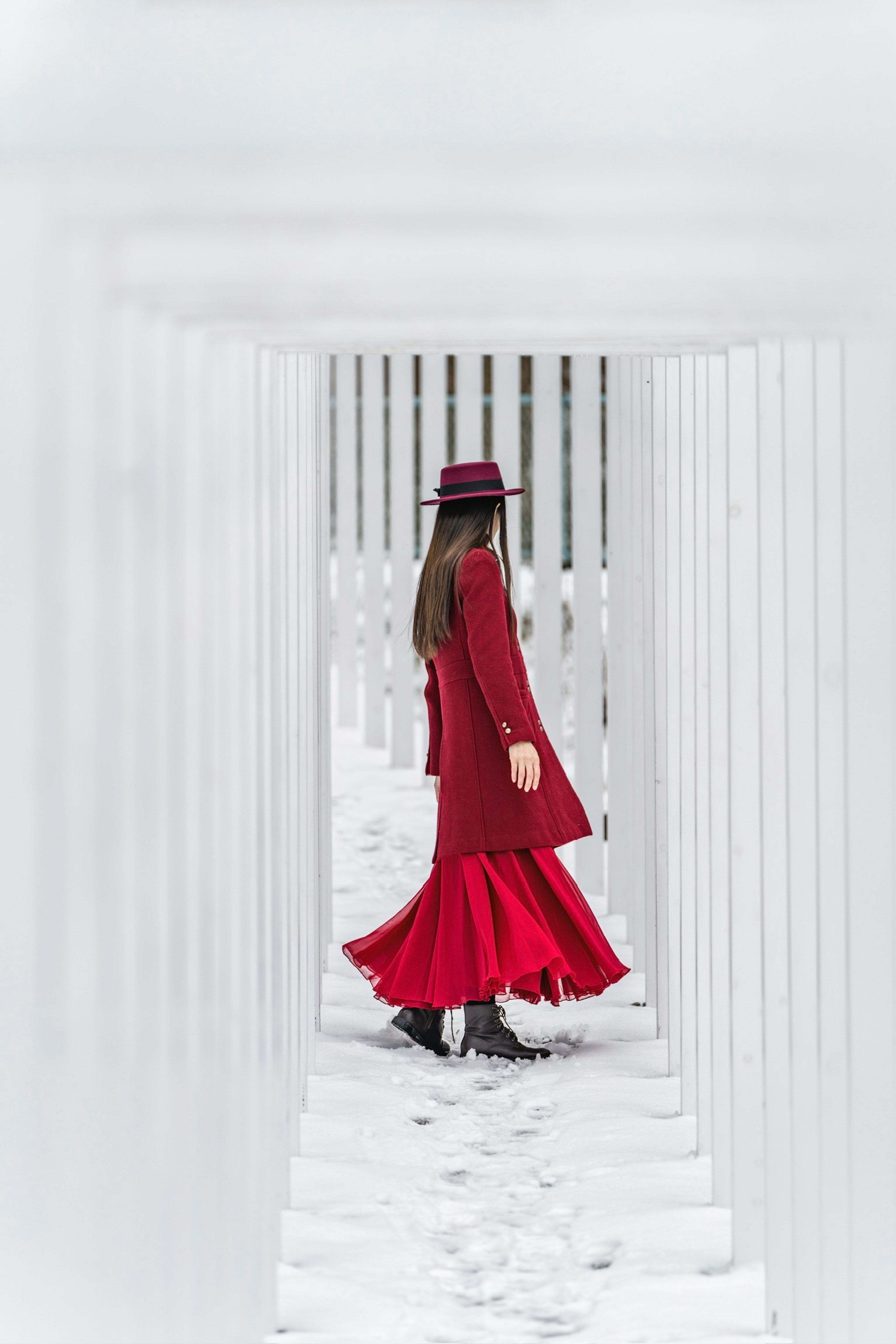 Una donna in abito rosso che cammina attraverso un tunnel di colonne bianche nella neve