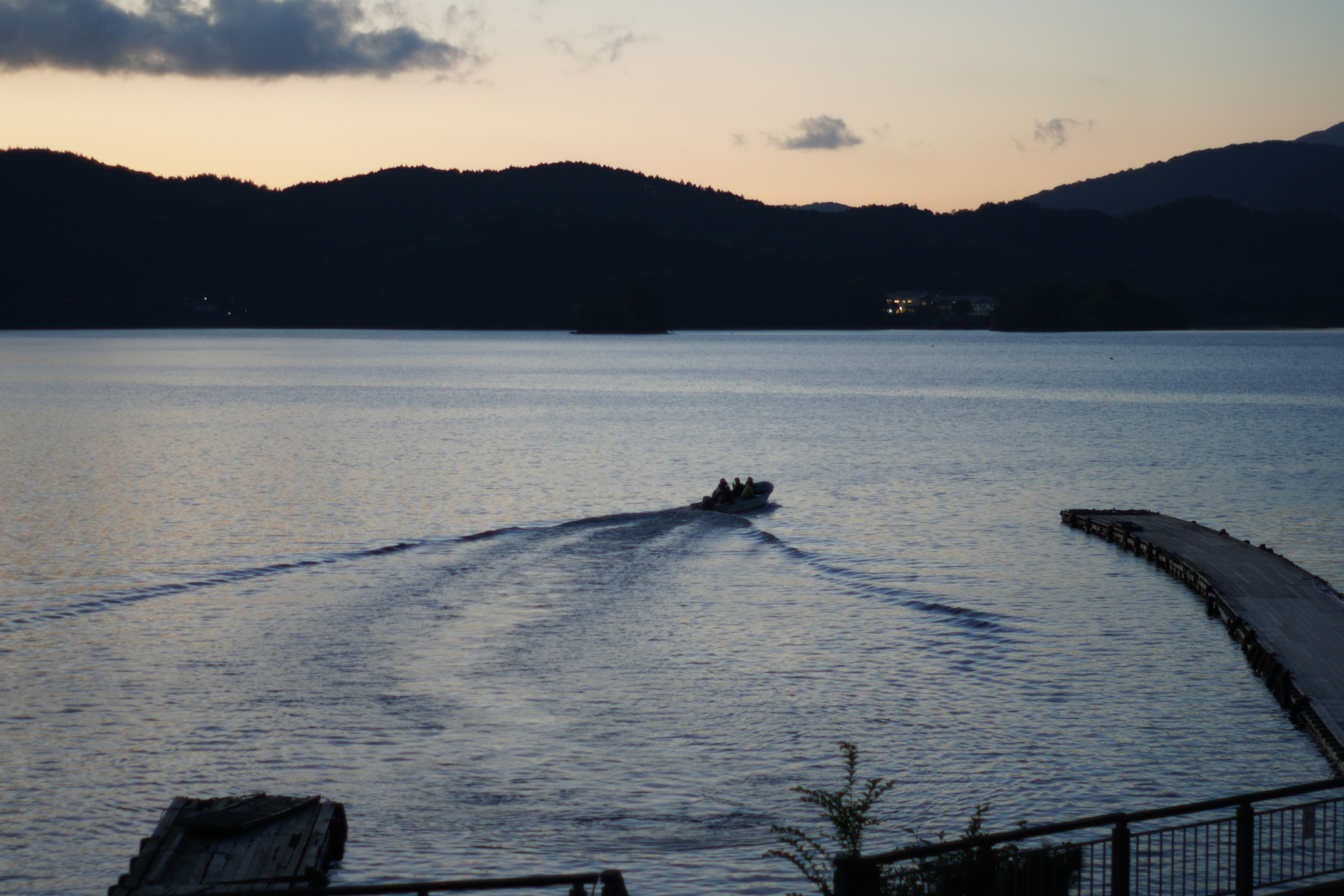 静かな湖にボートが進む夕暮れの風景で、山々が背景に広がっている