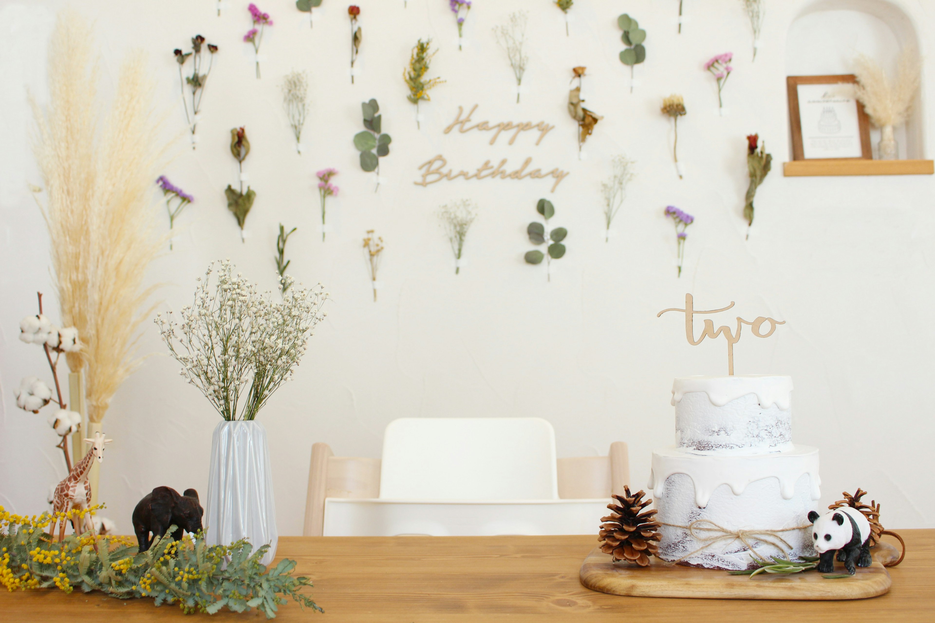 Allestimento per compleanno con una torta bianca e fiori secchi sul muro