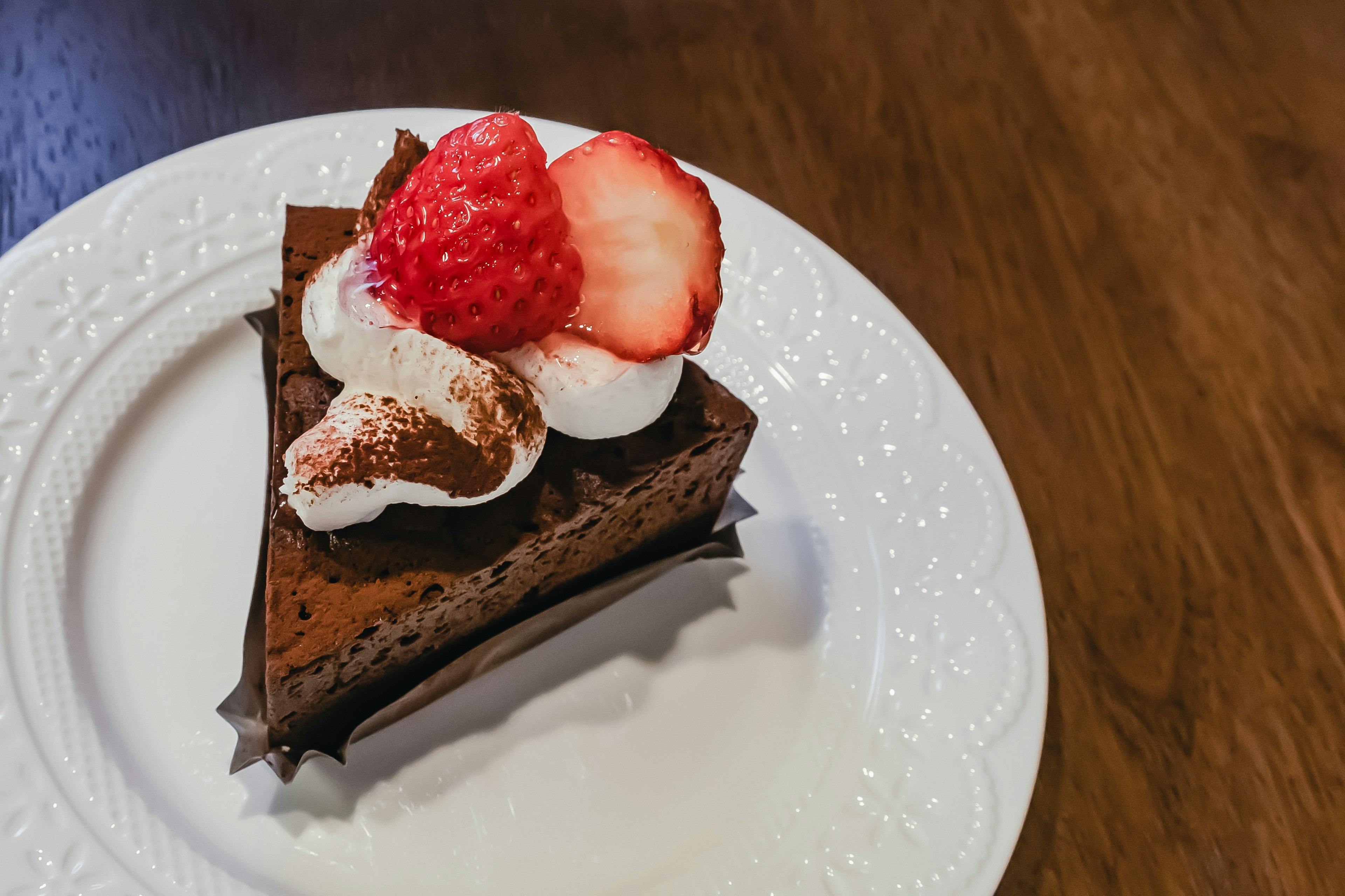 Fetta di torta al cioccolato guarnita con panna e fragole fresche su un piatto bianco