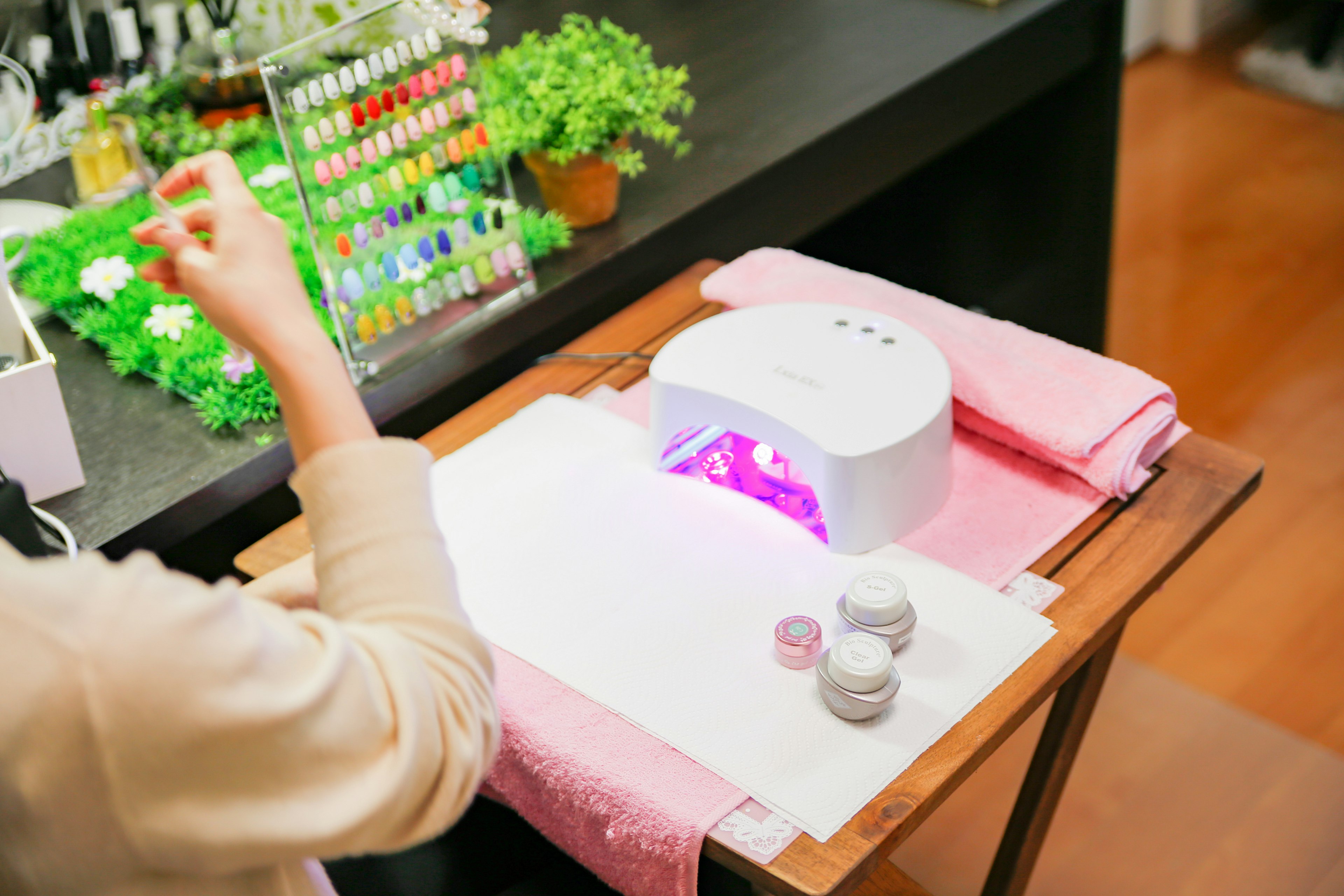 Nail salon scene with a hand applying nail polish using a UV lamp and colorful nail polishes