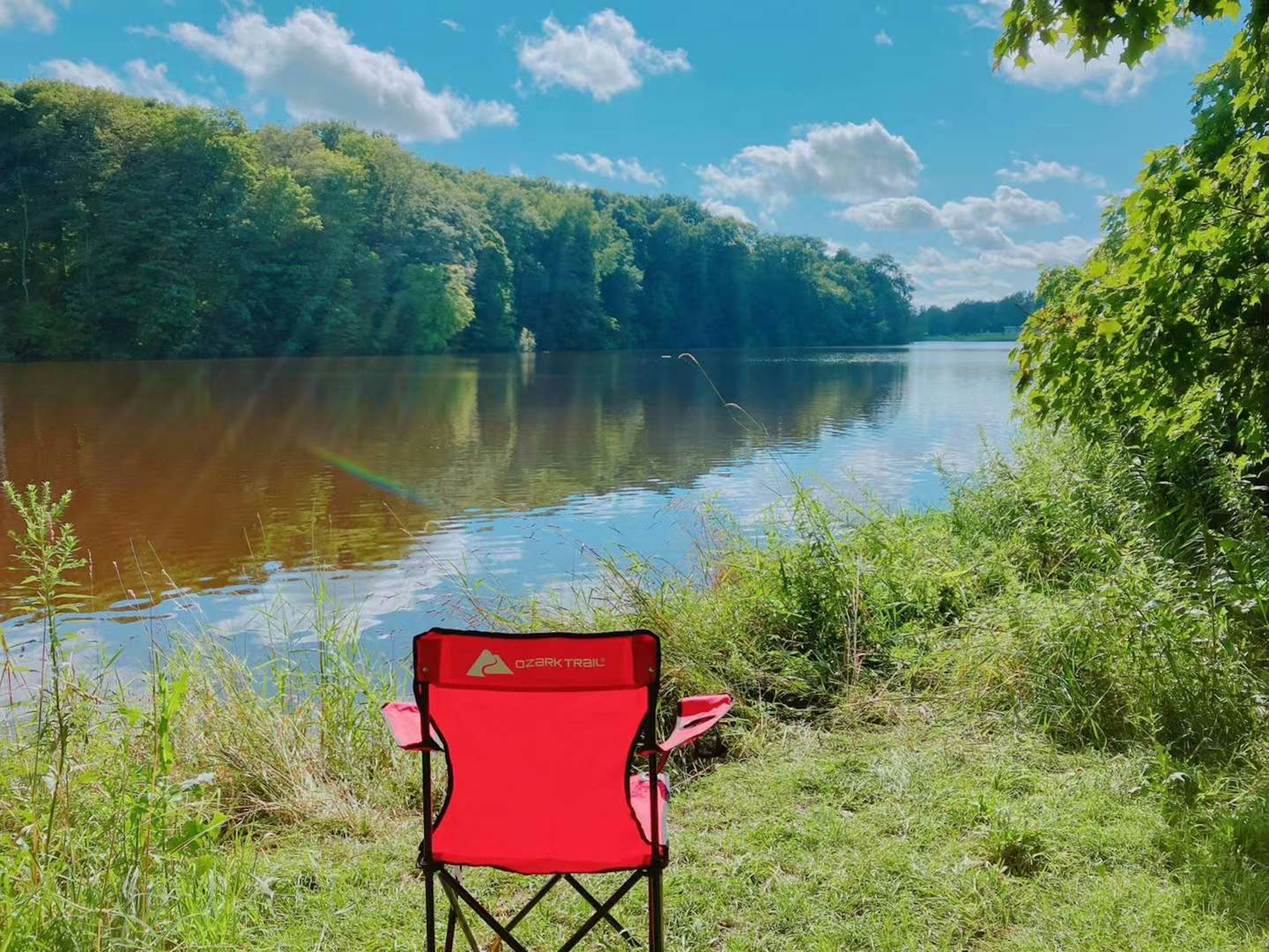 A red chair positioned by the riverside with a beautiful natural landscape