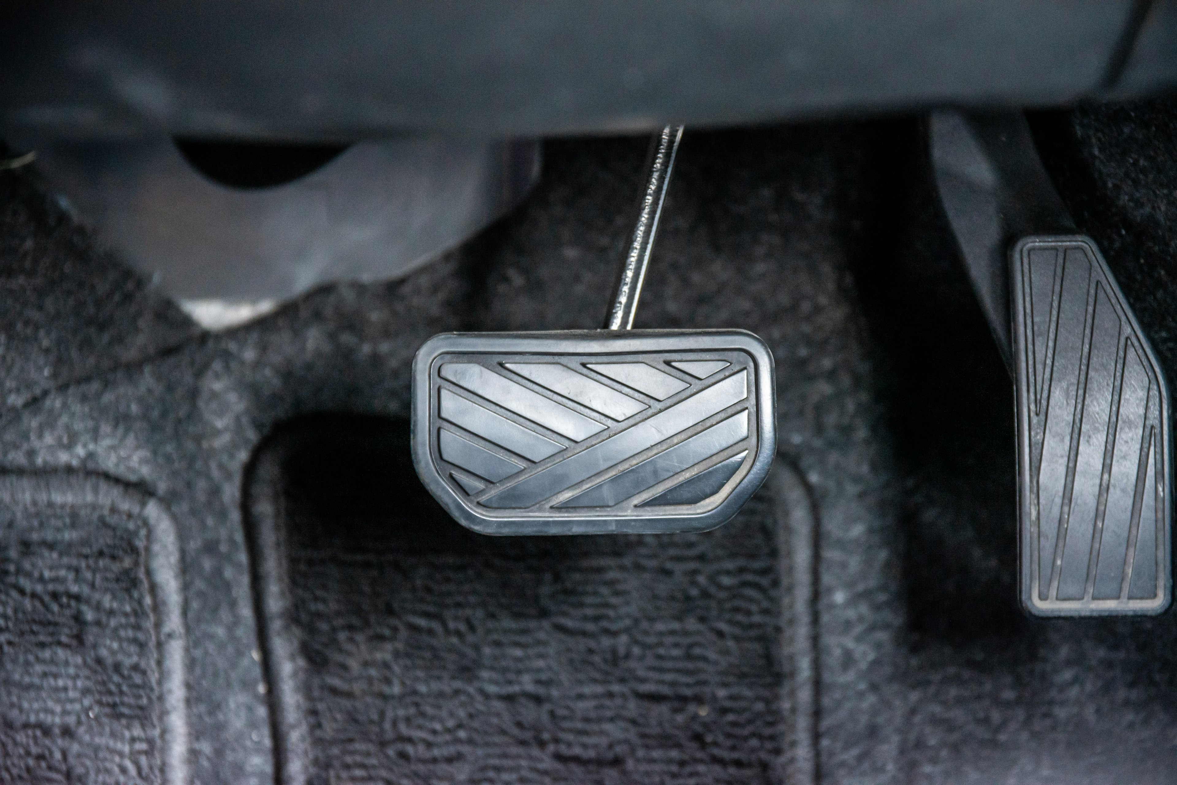 Close-up image of a car pedal featuring a unique pattern with black carpeting in the background