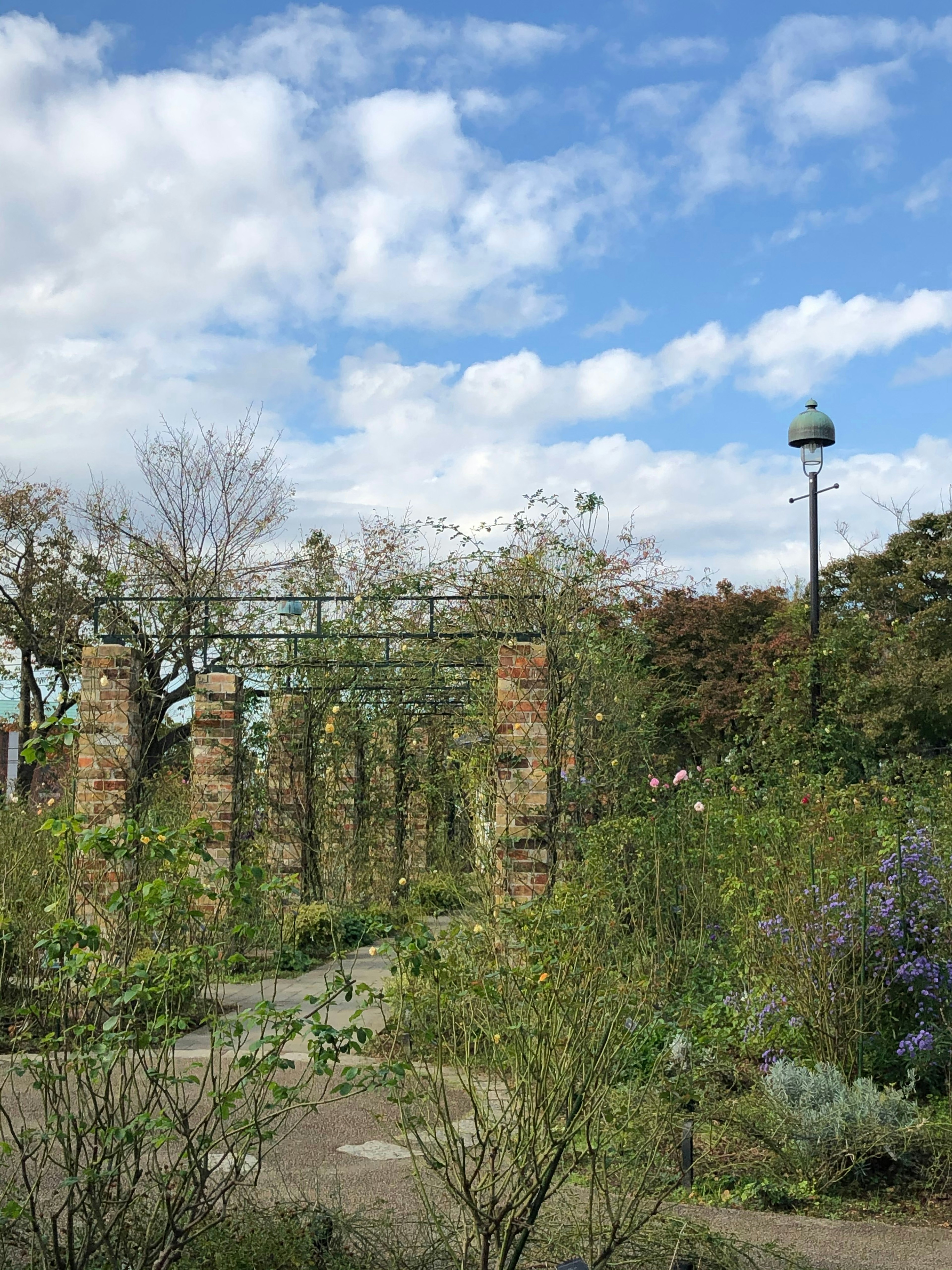 Scène de jardin avec un ciel bleu et des nuages mettant en vedette des piliers en pierre et des plantes vertes