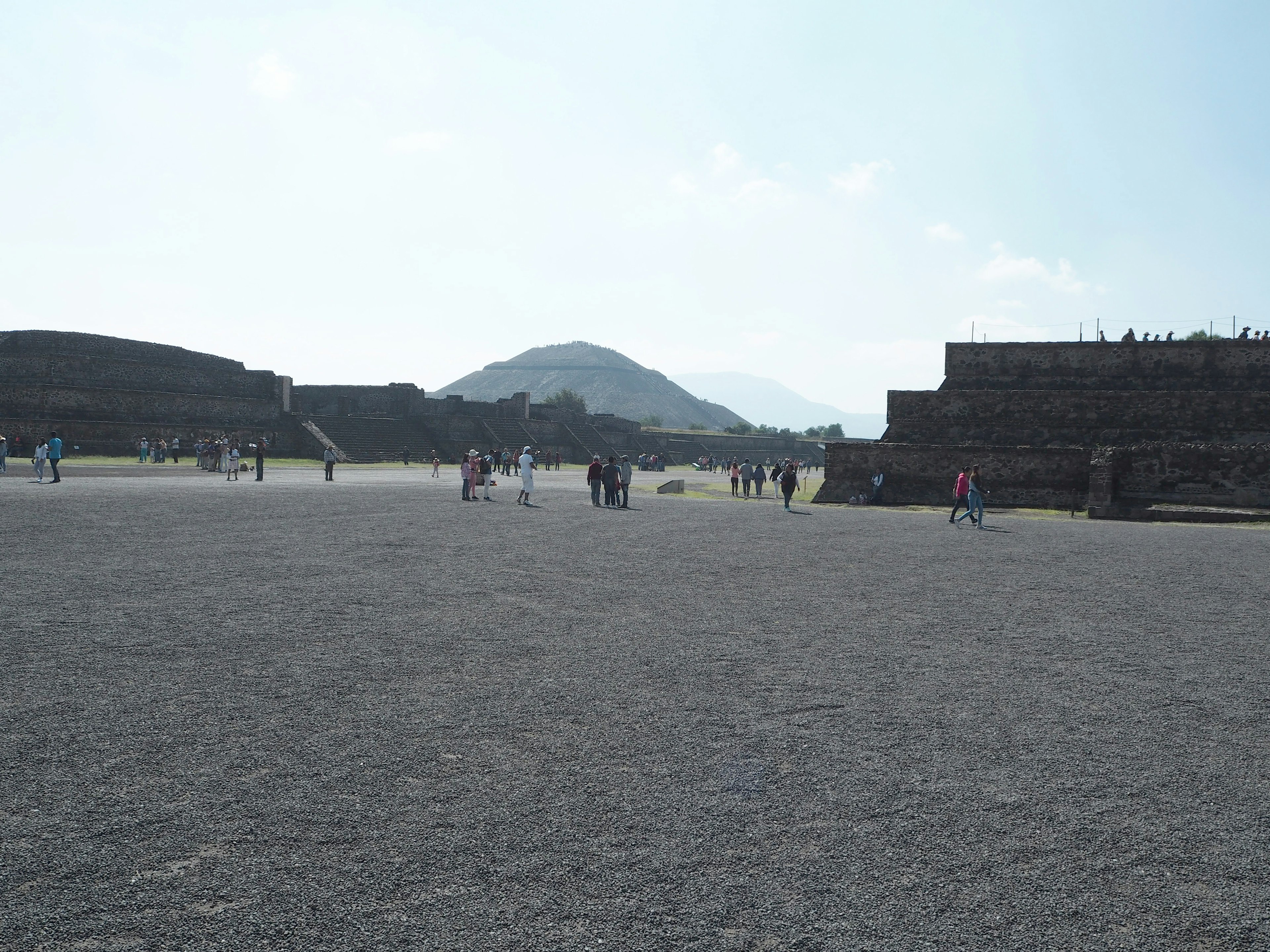 Vista de Teotihuacan con visitantes caminando sobre una superficie de grava