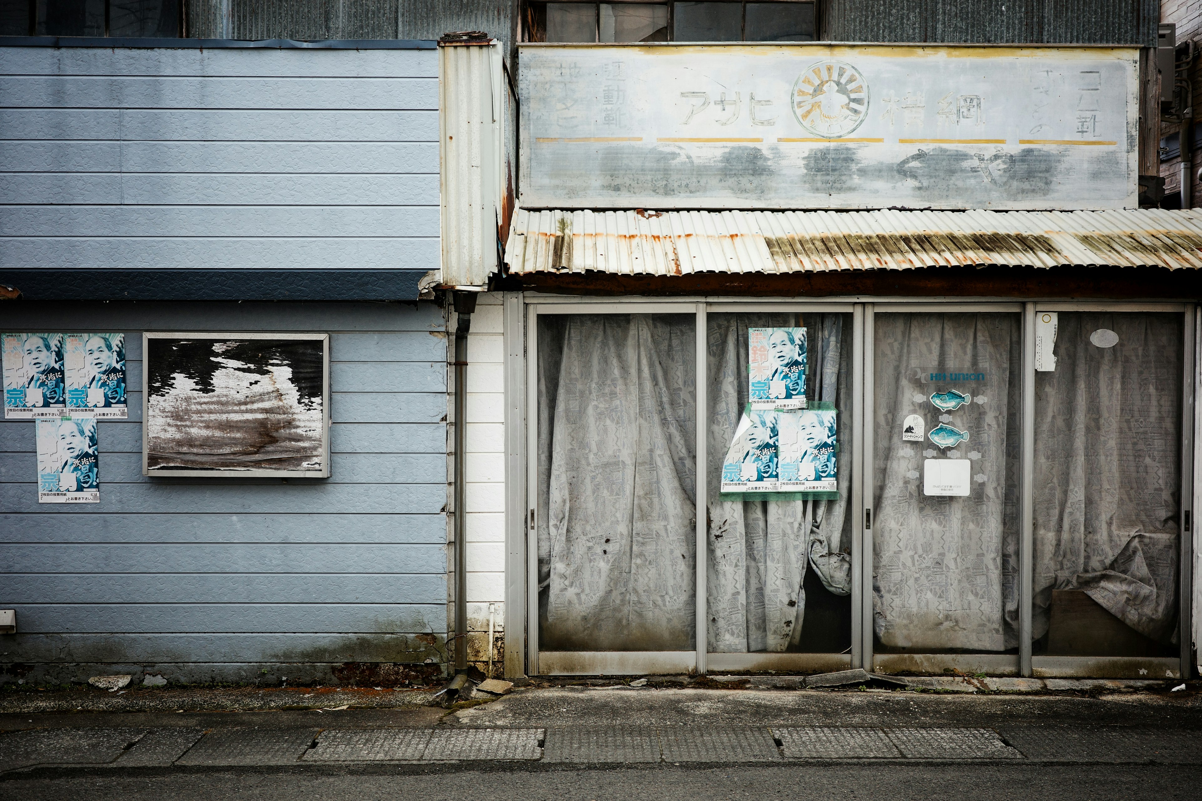 Exterior of an old building with tattered curtains and faded posters on the wall