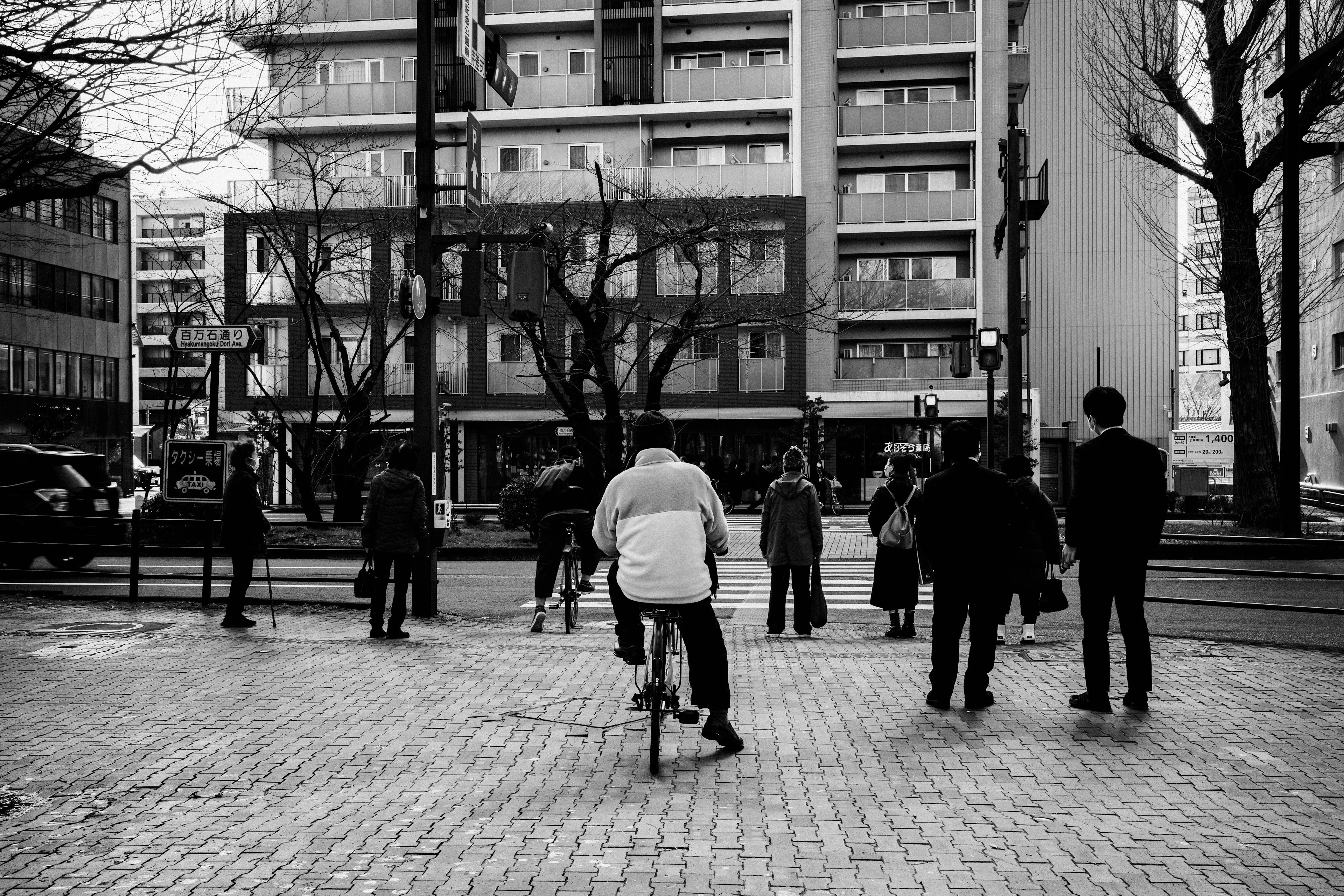 Scena urbana in bianco e nero con persone riunite una persona in bicicletta e edifici visibili