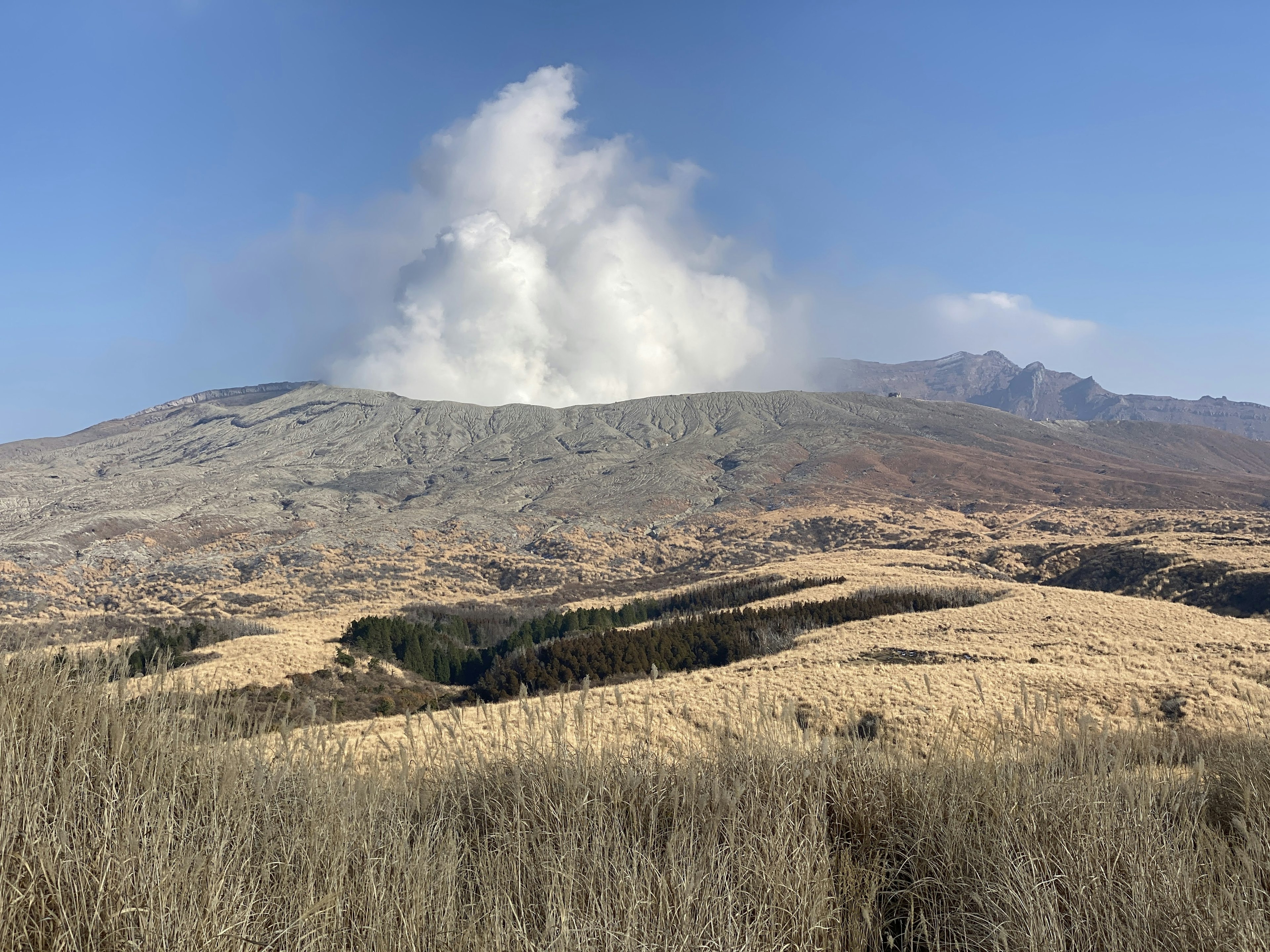 Paisaje con humo volcánico elevándose sobre colinas y hierba seca