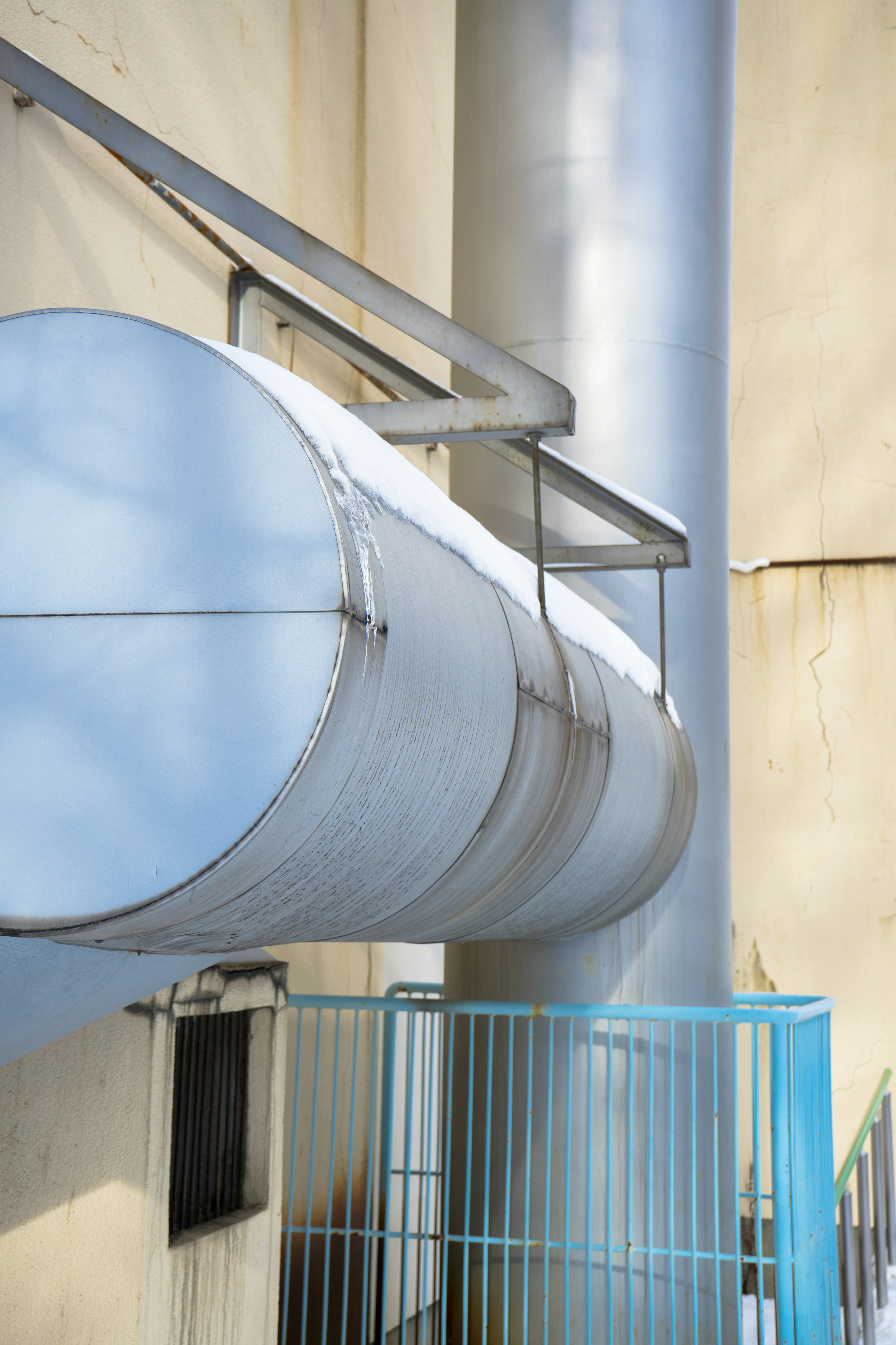 Industrial structure featuring metallic pipes and a blue fence