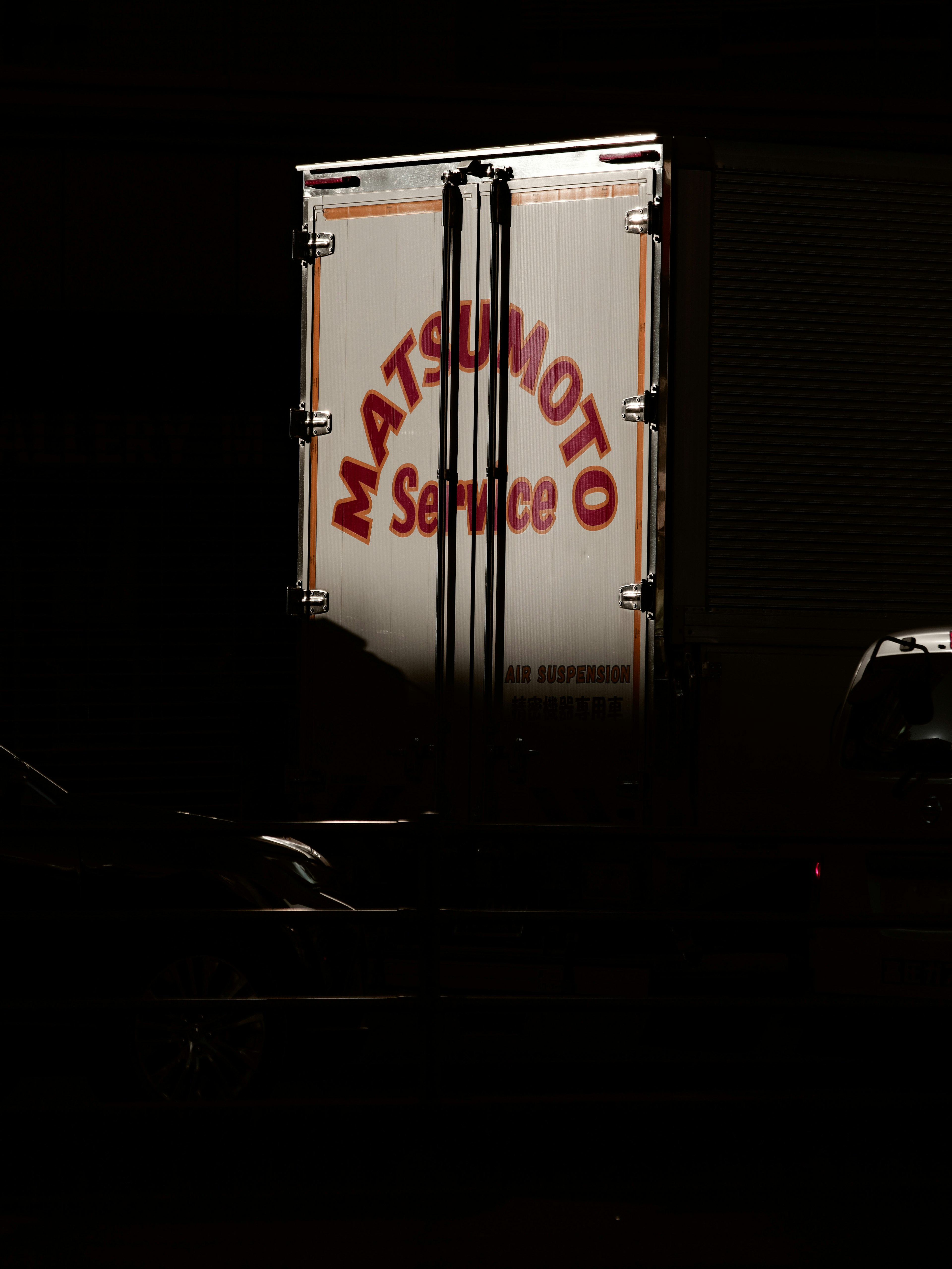 Arrière d'un camion avec le logo Matsumoto Service éclairé sur un fond sombre