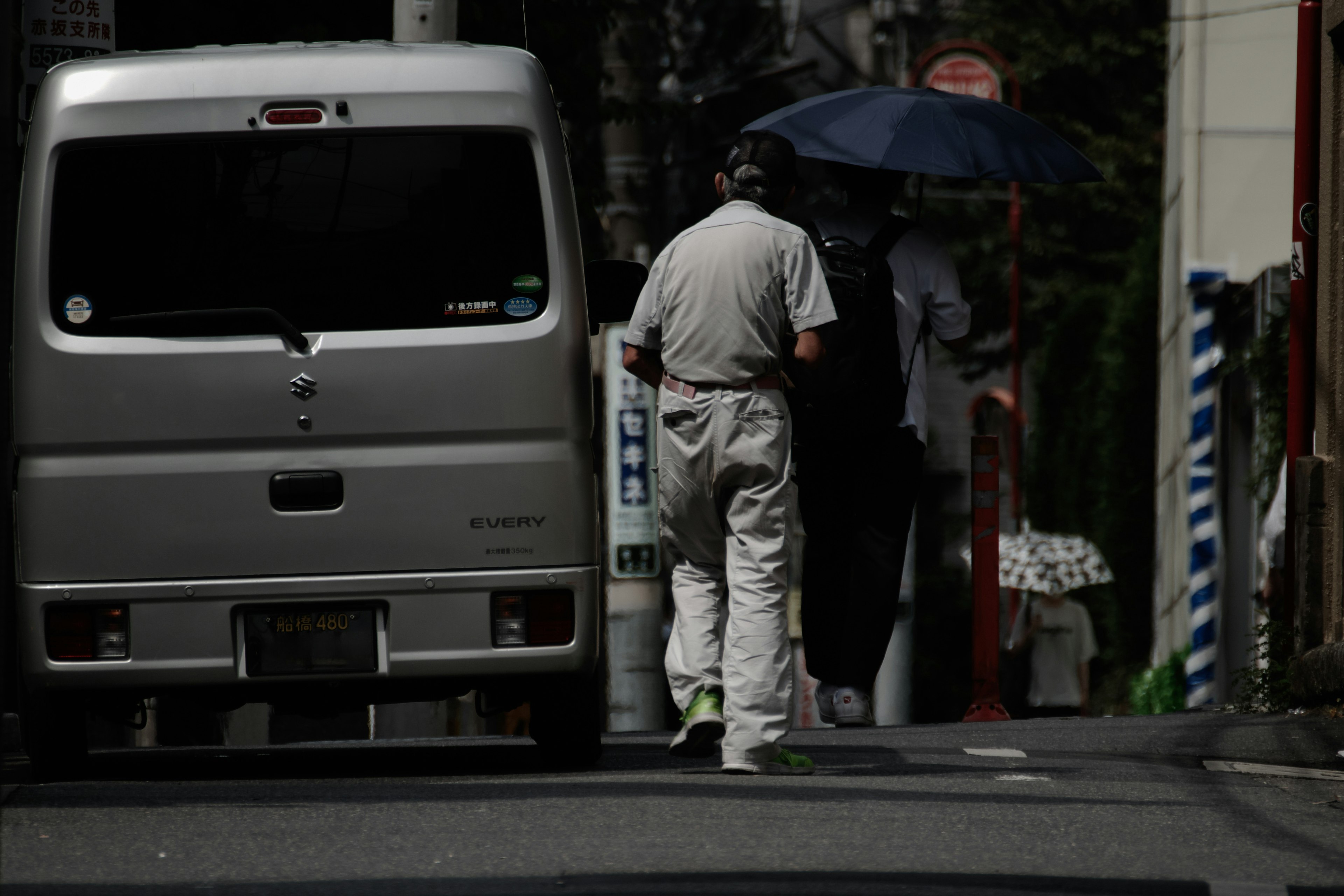 人が傘を持って歩いている街の風景 車が停まっている