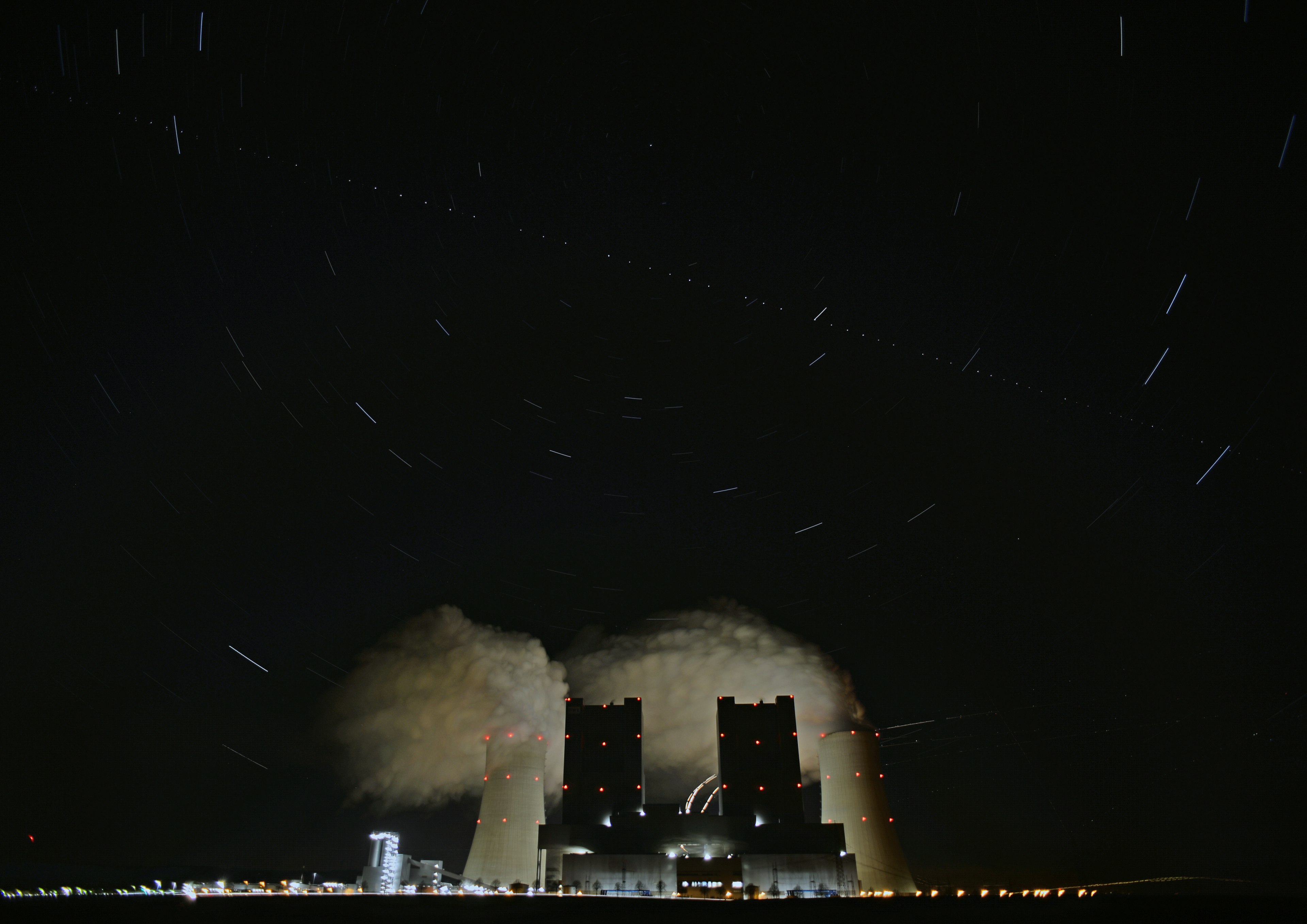 Launch pad emitting smoke under star trails in the night sky