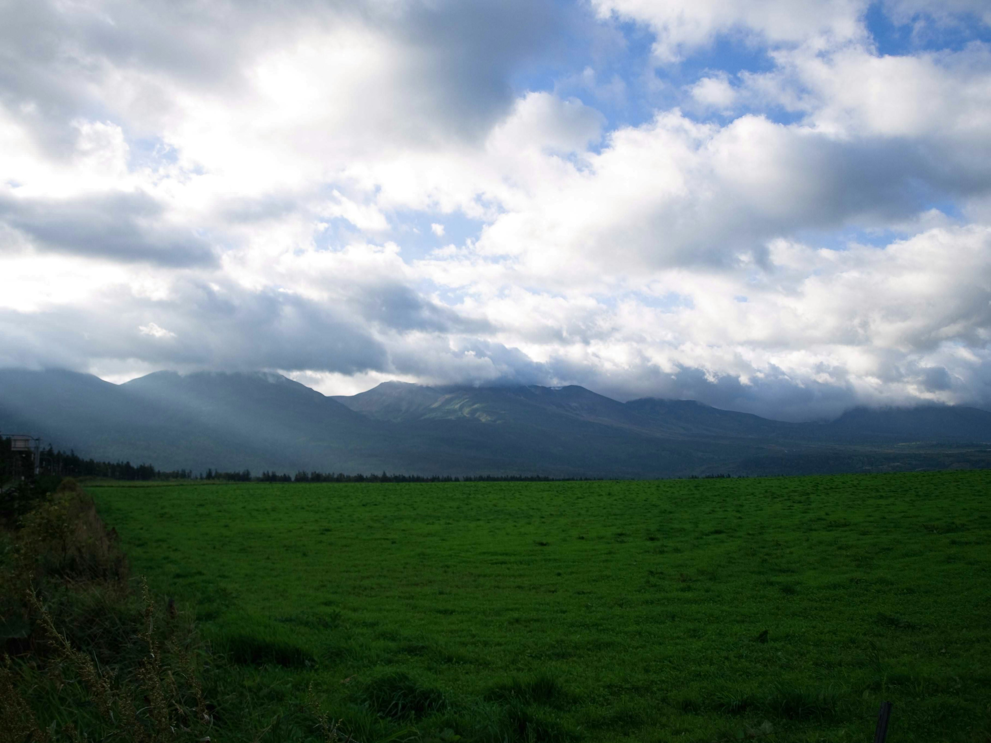 Pradera verde con montañas bajo un cielo azul y nubes