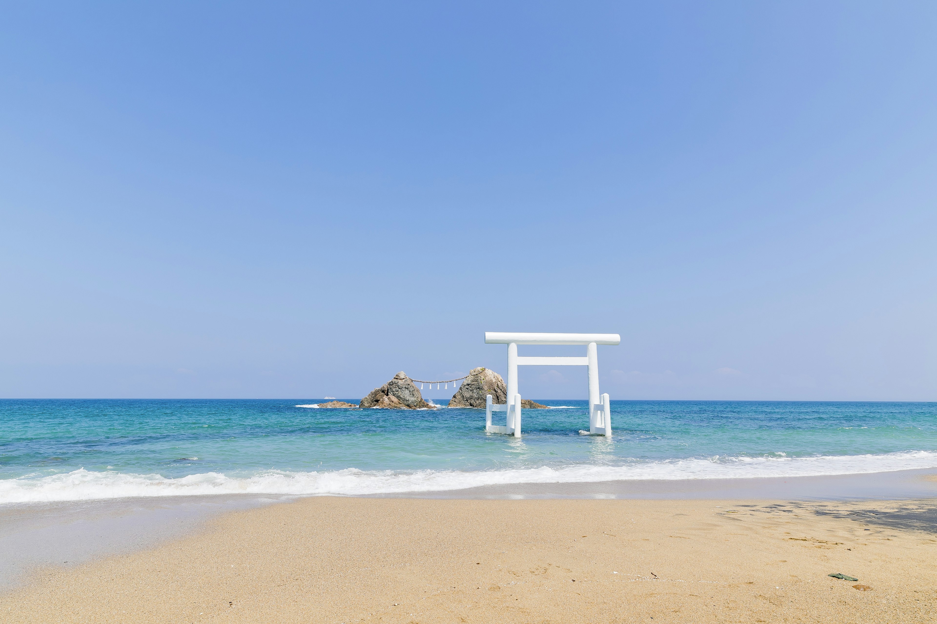 Beautiful beach scene with a white torii gate under a blue sky and sea