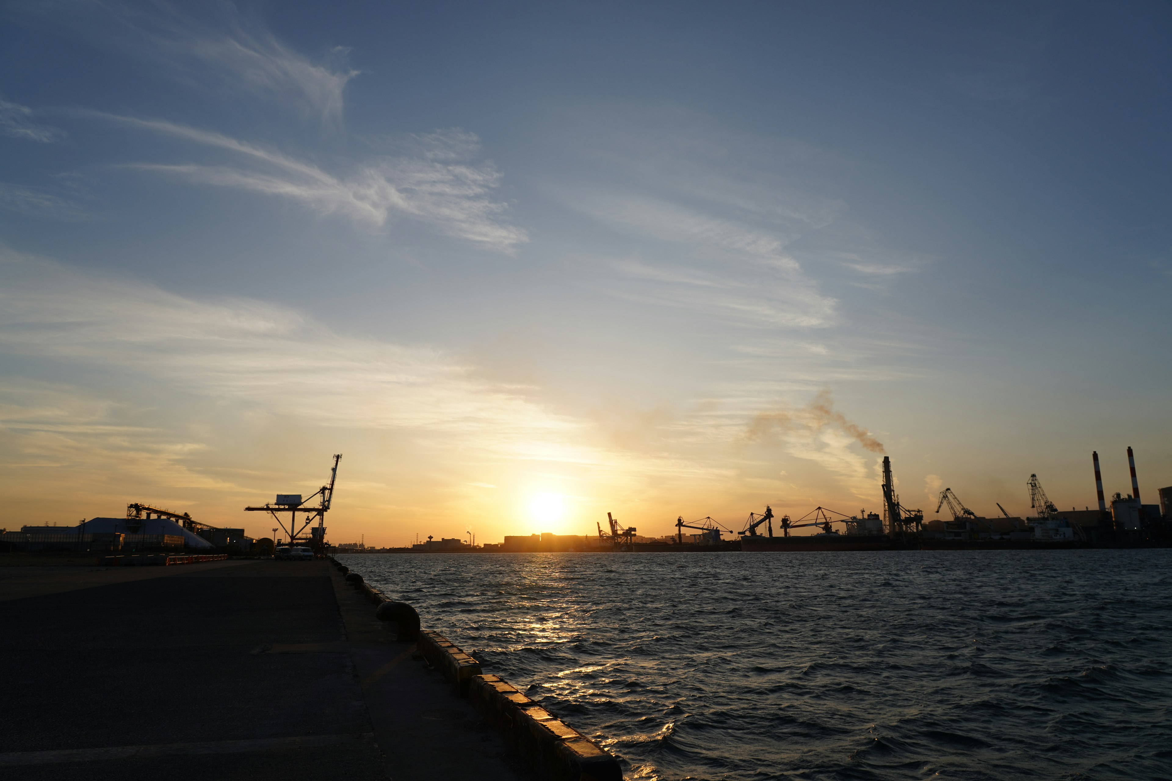 港の夕日と工業設備のシルエットが見える風景