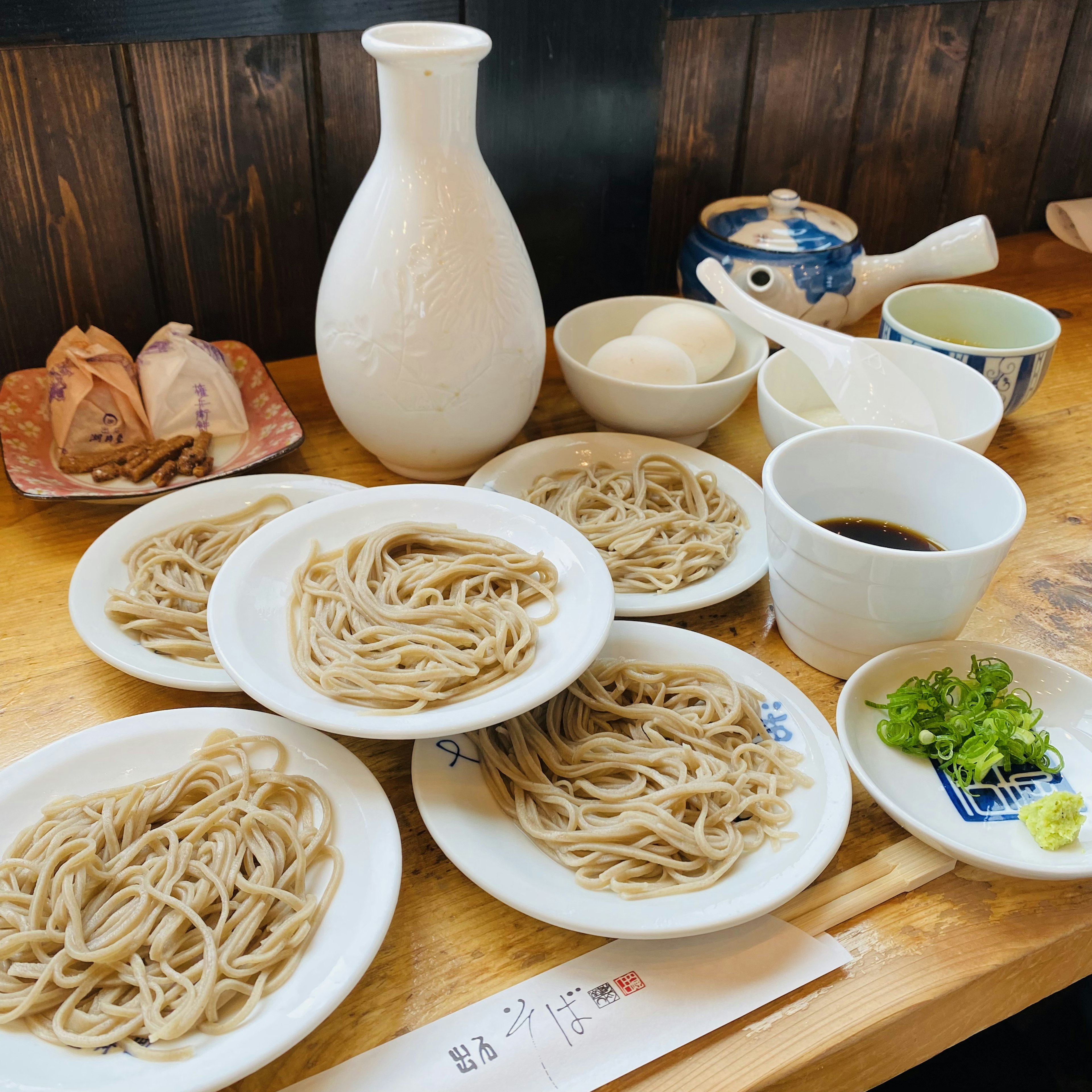 Table set with soba noodles and sake featuring various bowls and garnishes