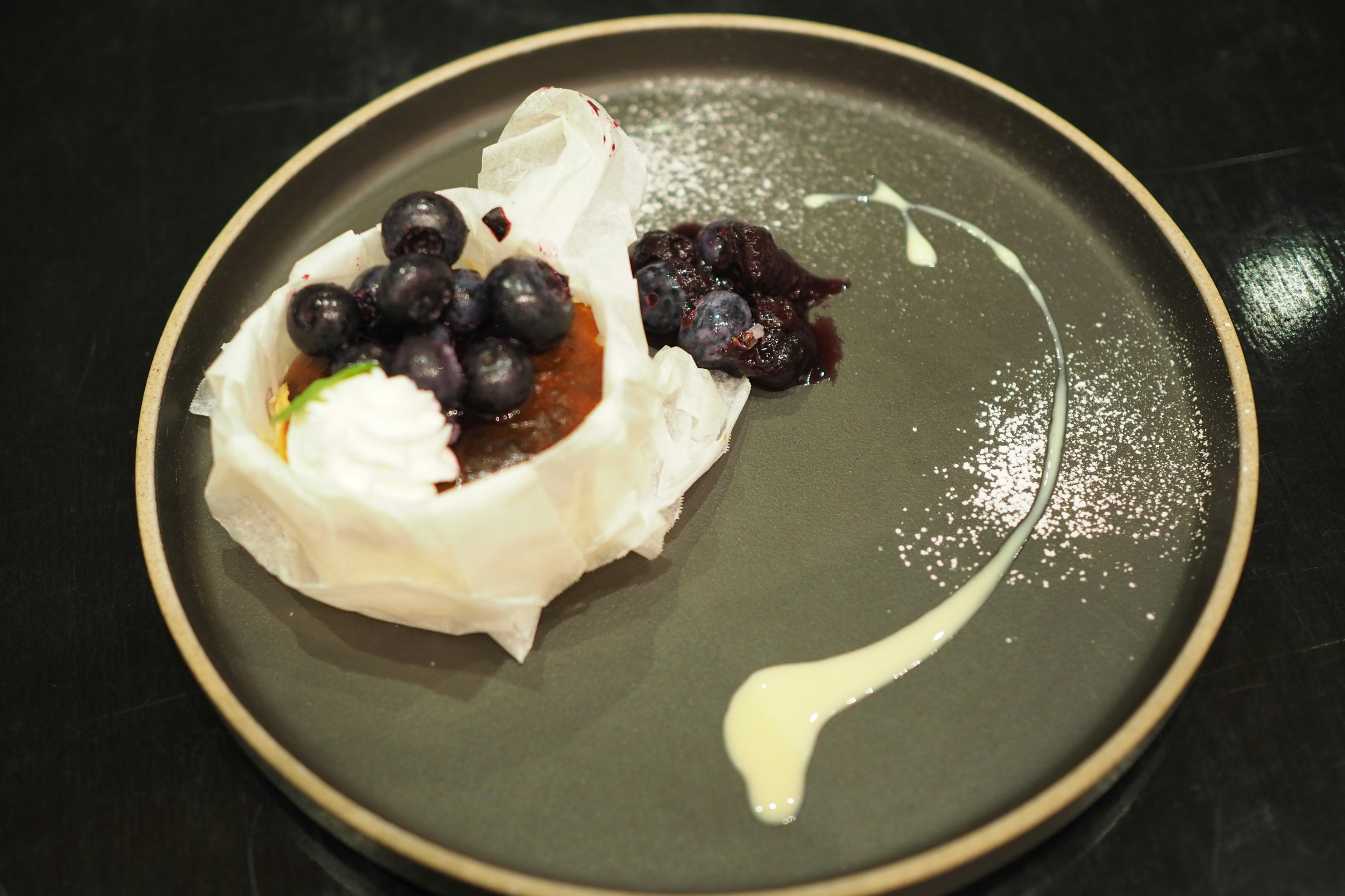 Dessert auf einem schwarzen Teller mit Blaubeeren und Sahne garniert