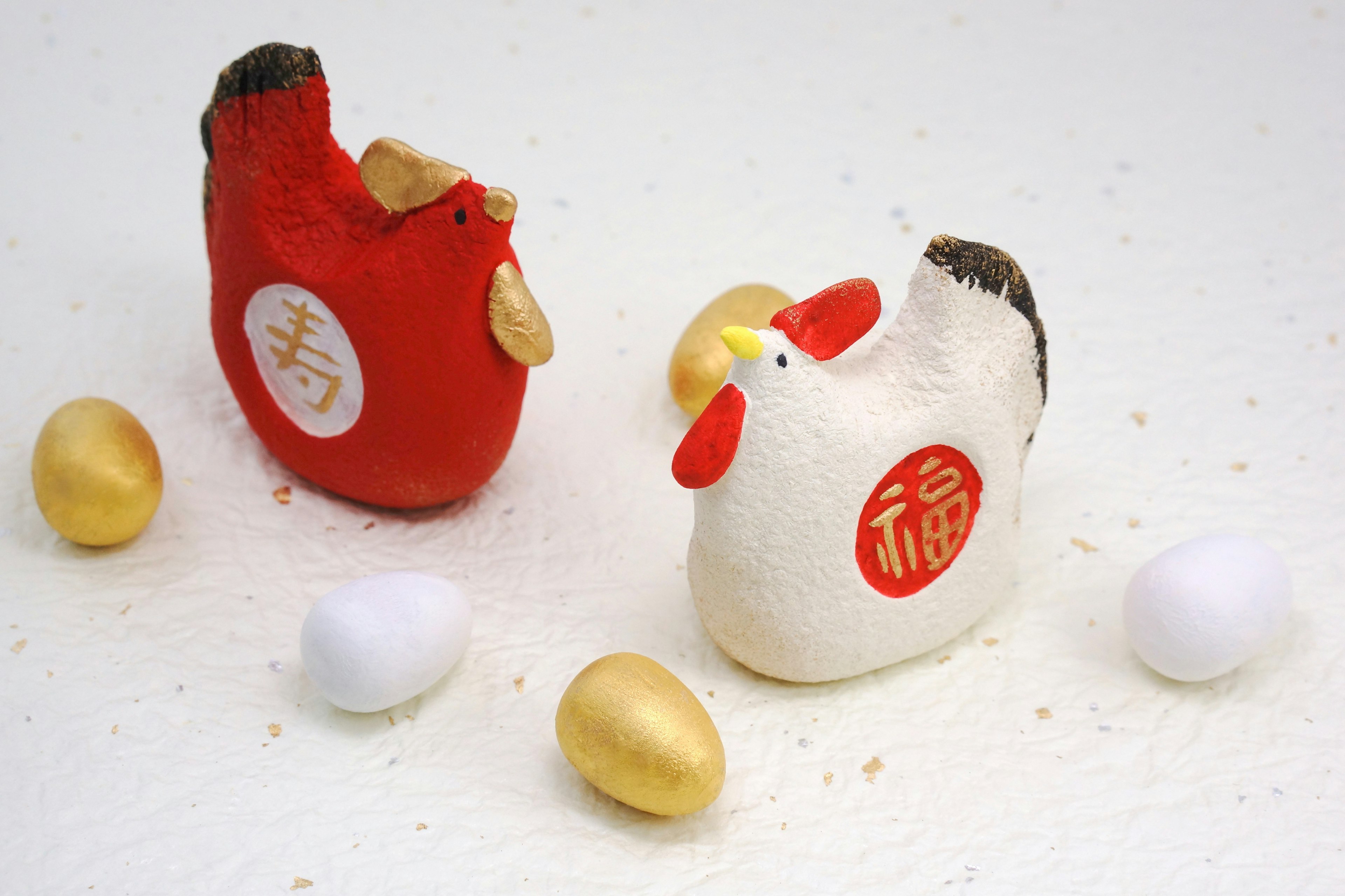 Image featuring red and white chicken figurines surrounded by golden and white eggs