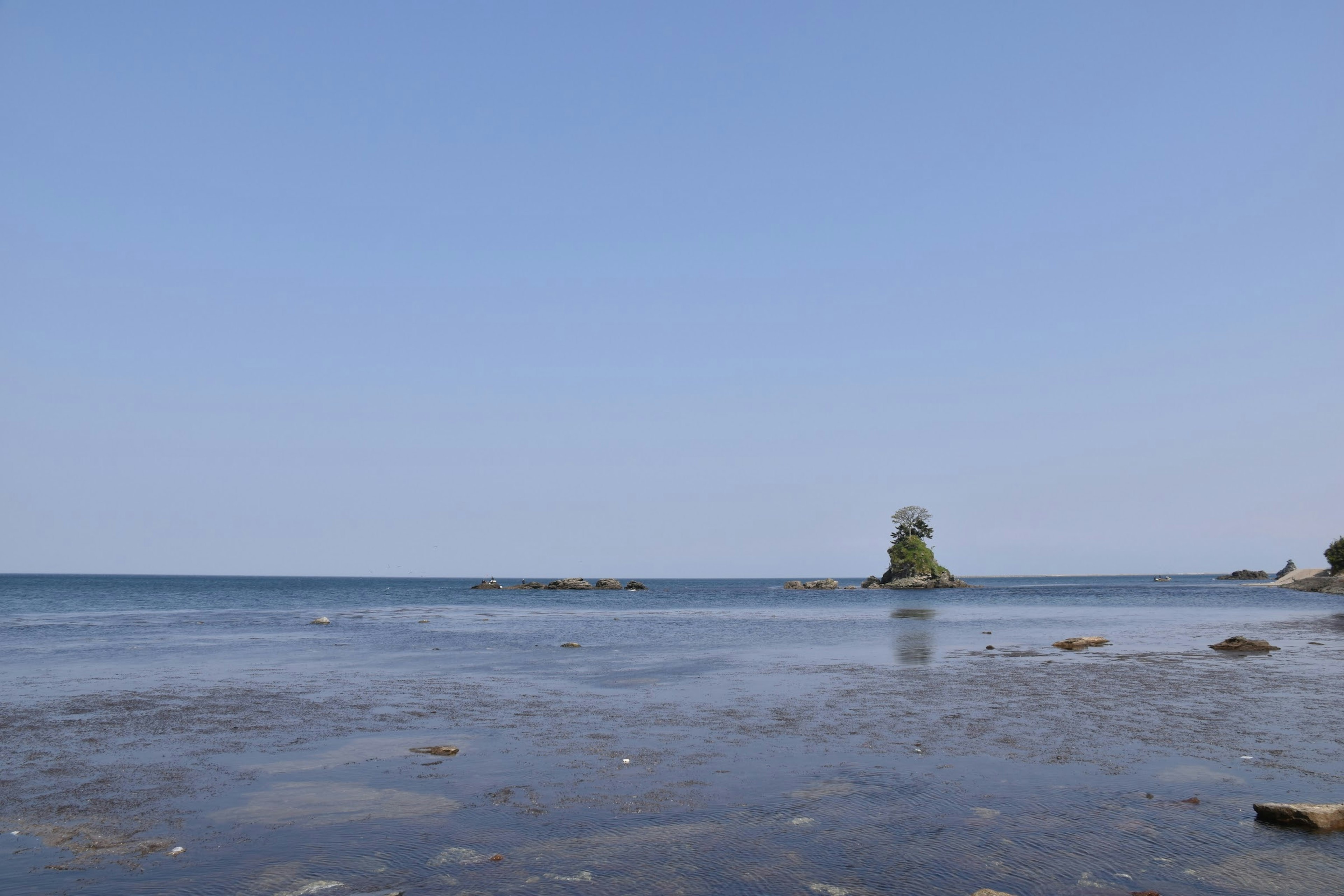 Calm sea with blue sky featuring a small island and rocks