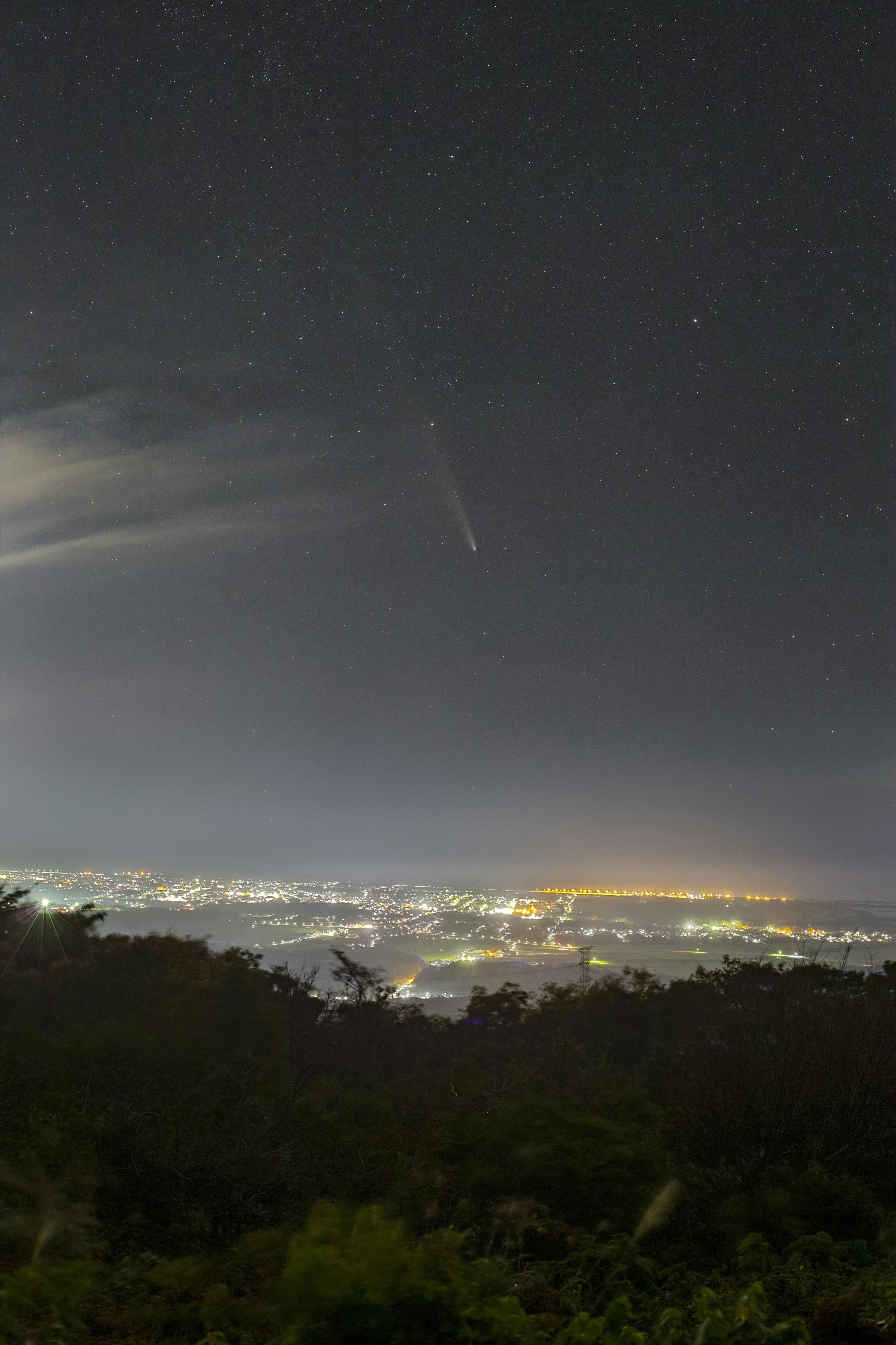 夜空に輝く星々と町の明かりが広がる風景に流れ星が見える