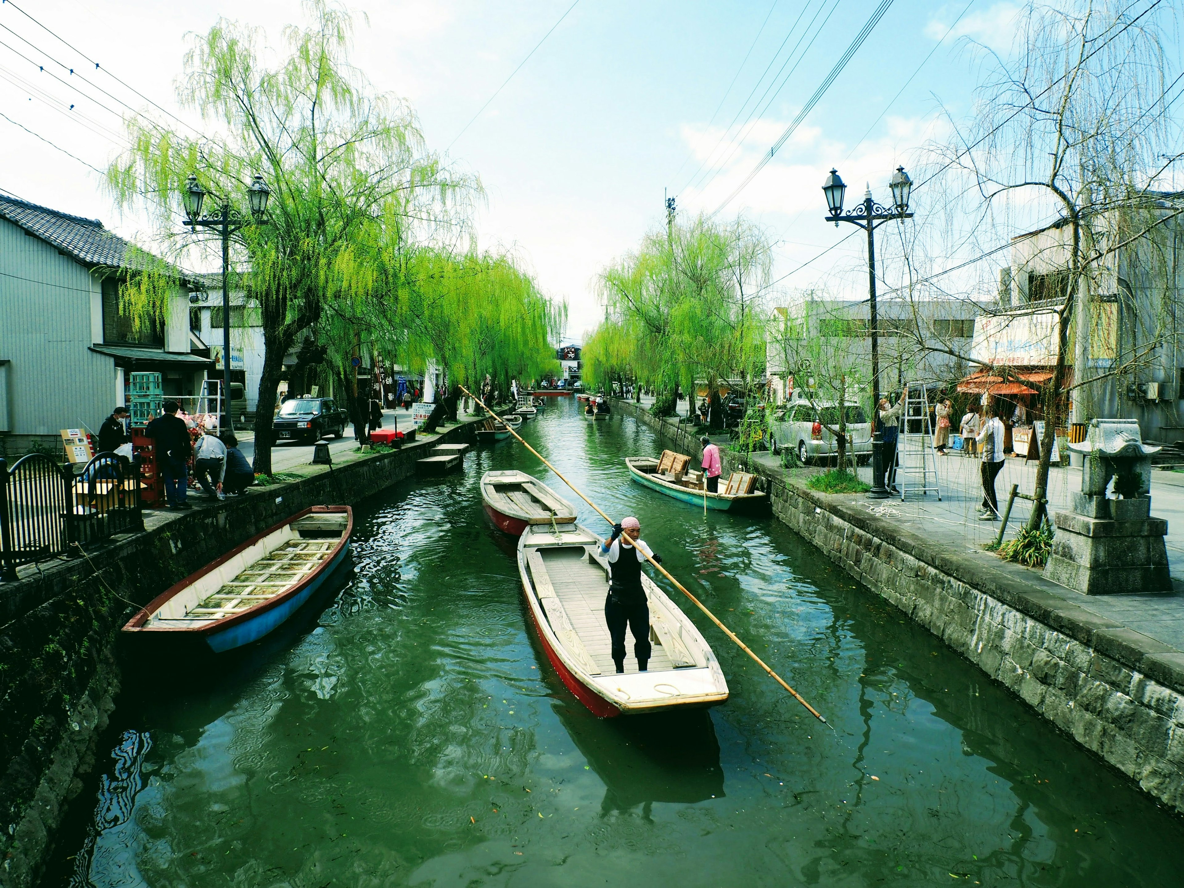 A fisherman rowing a boat on a tranquil canal surrounded by green willows