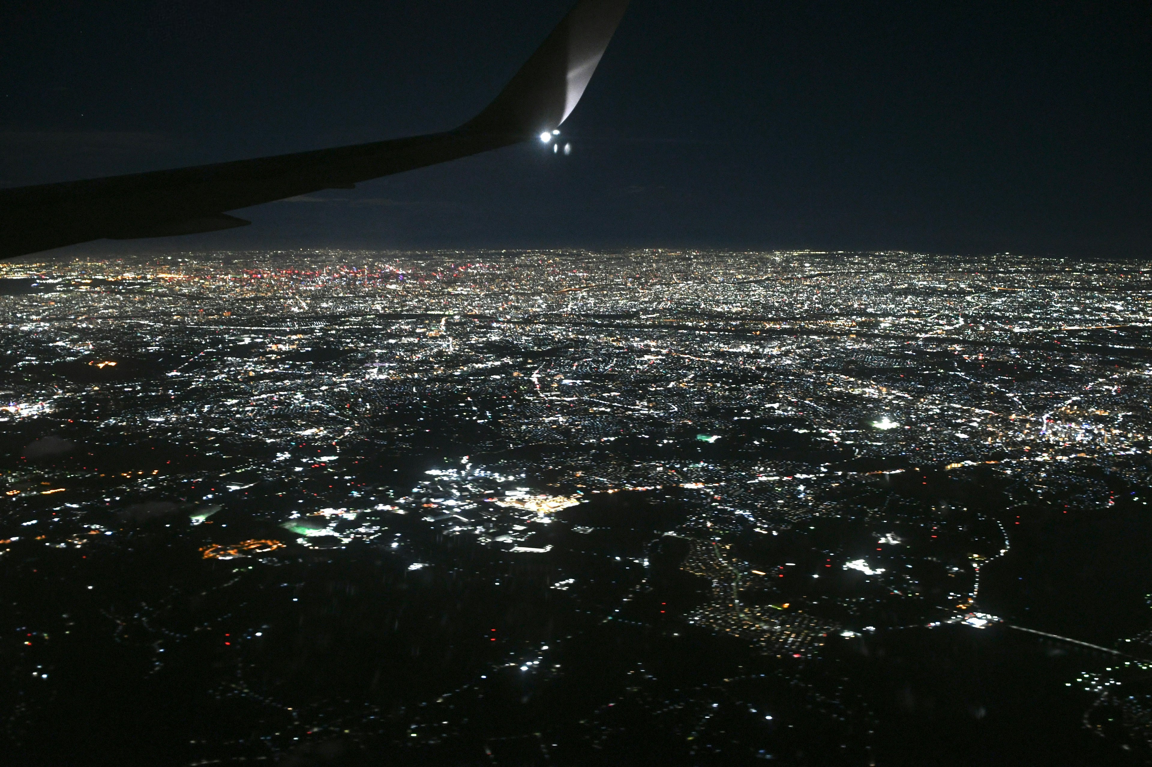 Vista aerea di un panorama urbano illuminato di notte con un'ala di aeroplano parzialmente visibile