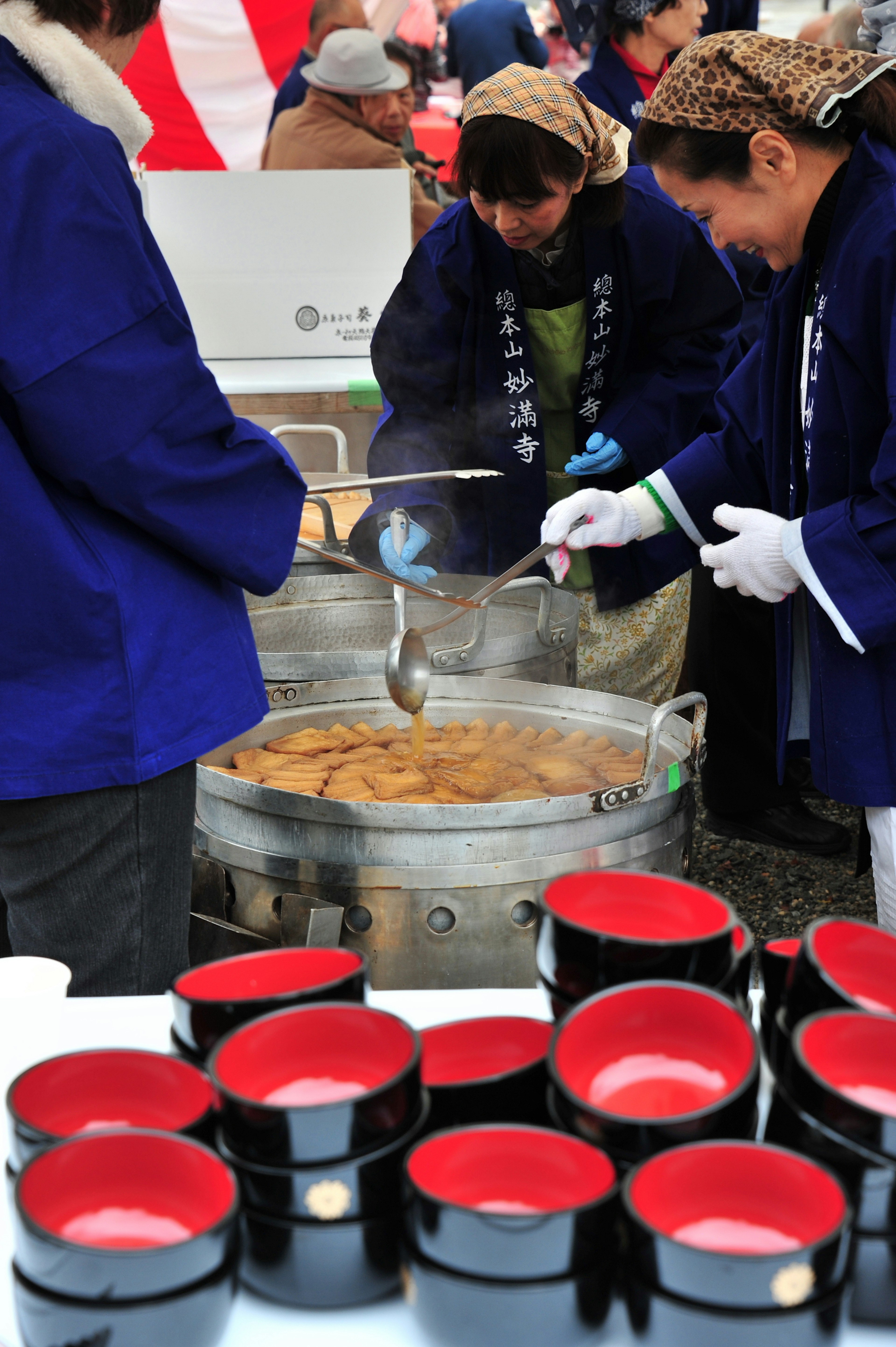 People in blue jackets serving food from a large pot