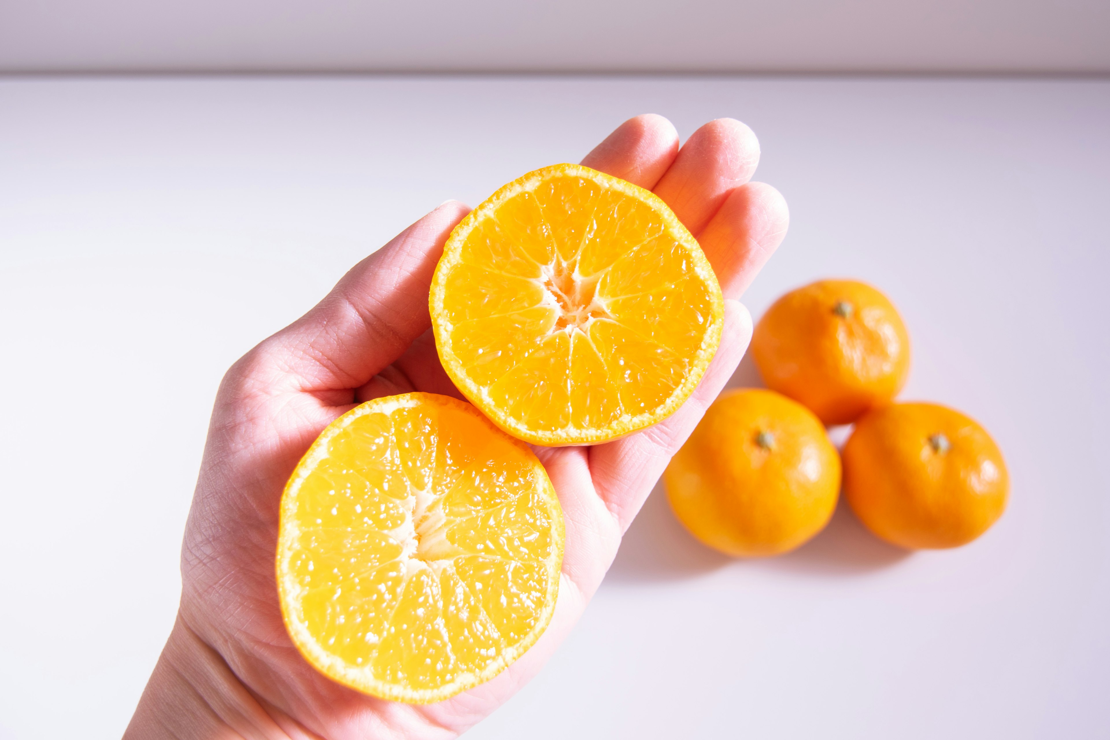 Eine Hand, die zwei Hälften einer Orange hält, mit drei ganzen Orangen im Hintergrund