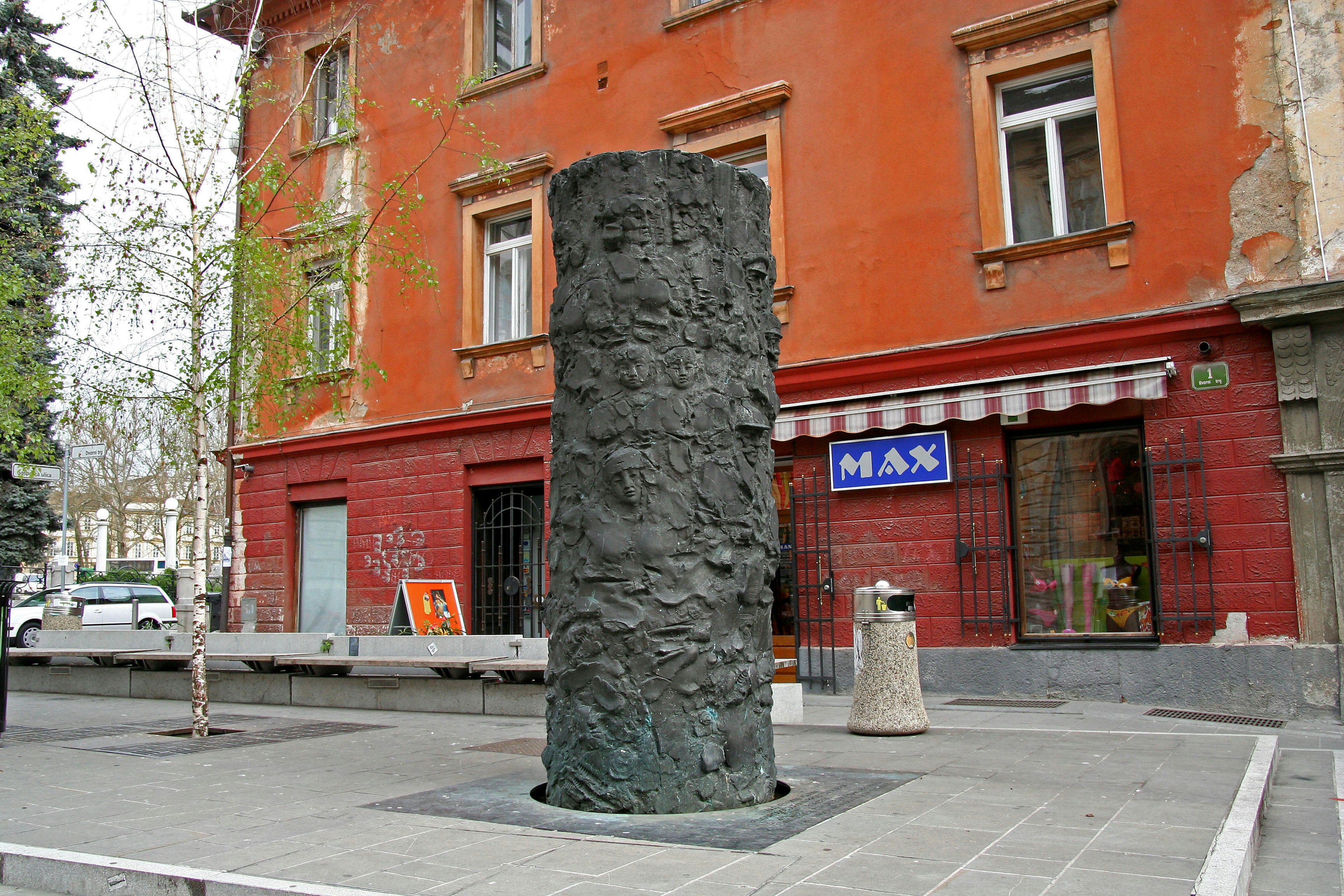 Eine schwarze skulpturale Säule vor einem roten Wandgebäude