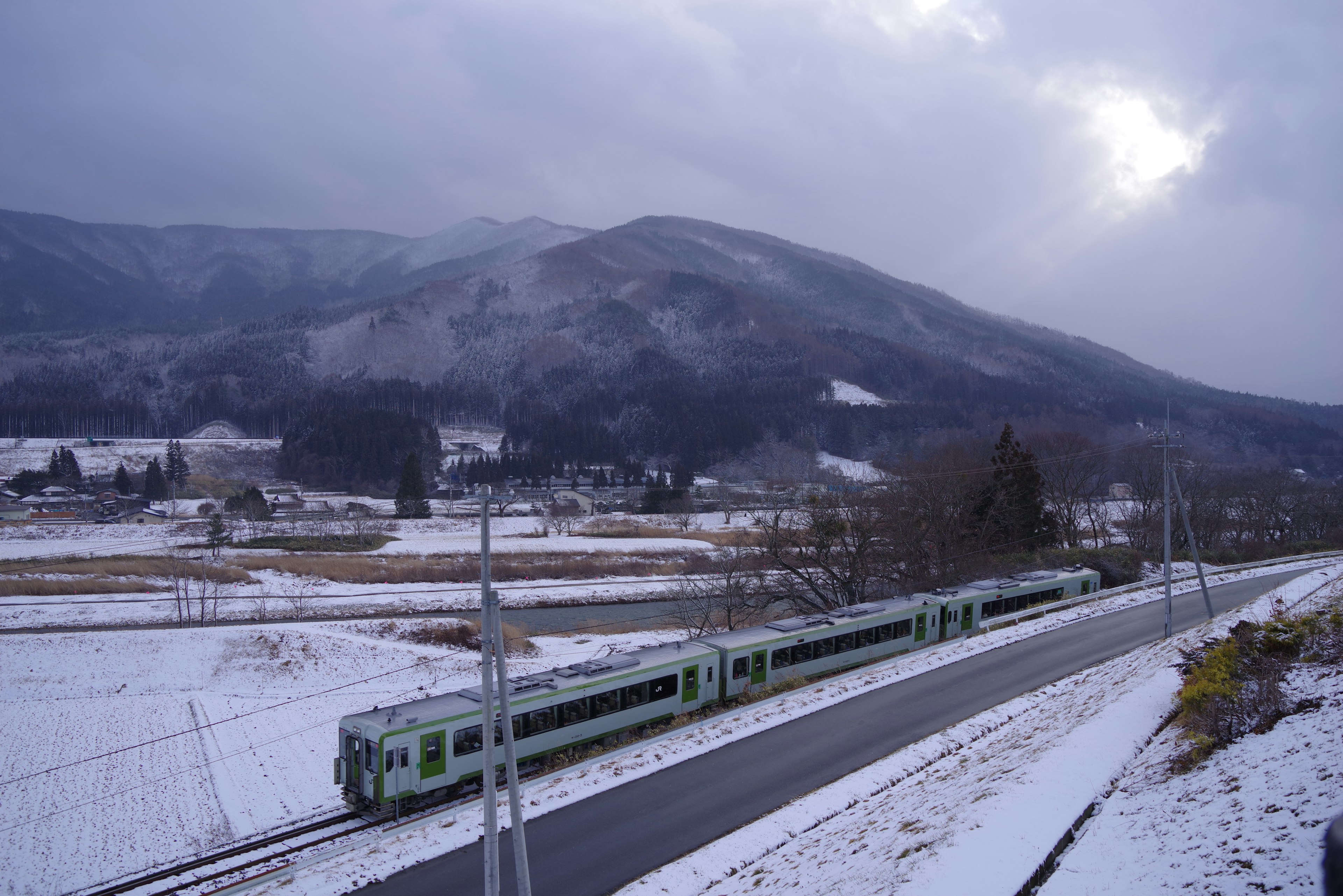 雪に覆われた風景を走る緑色の列車と山々