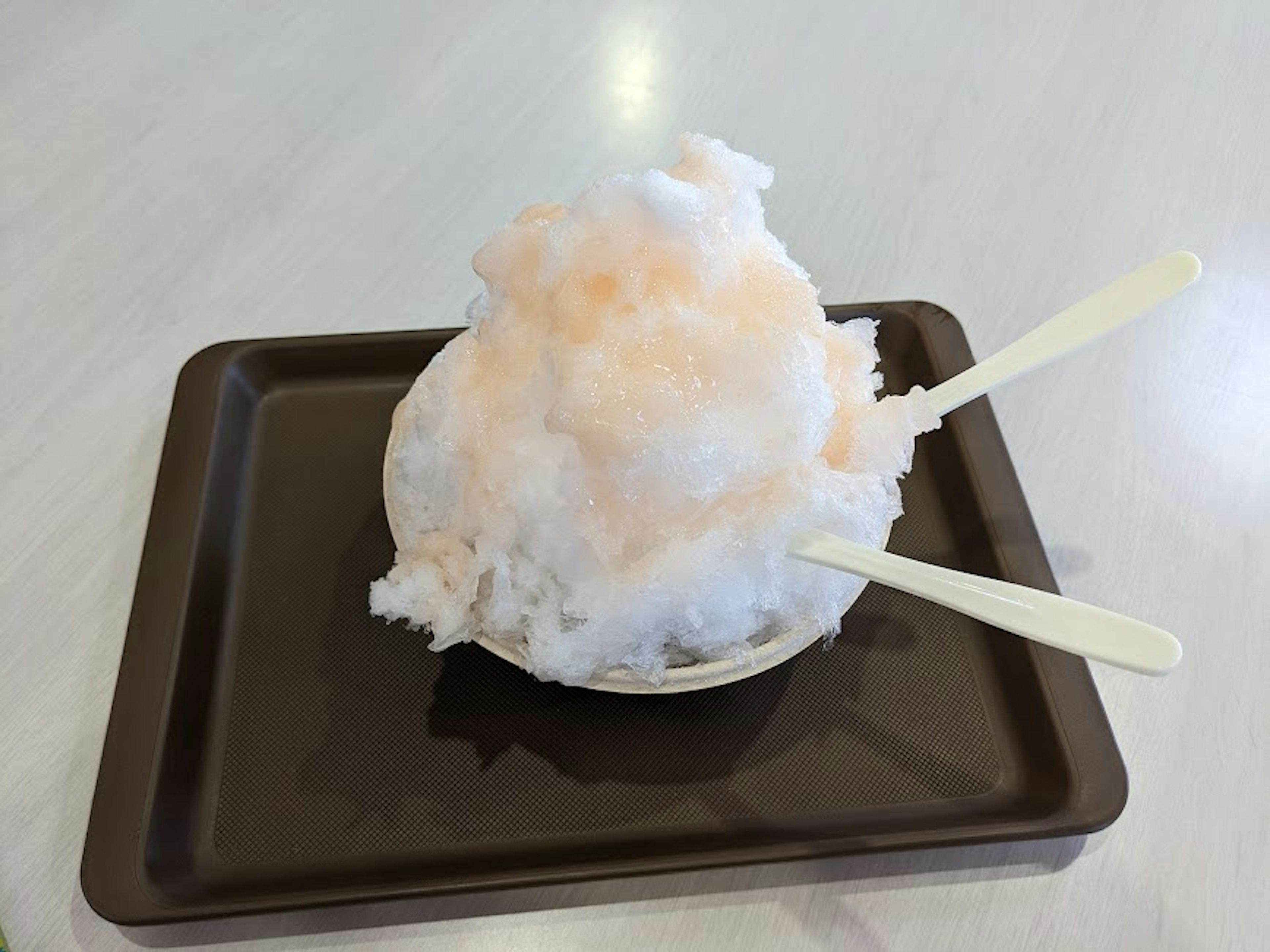 A bowl of fluffy ice shavings with a hint of pink on a brown tray