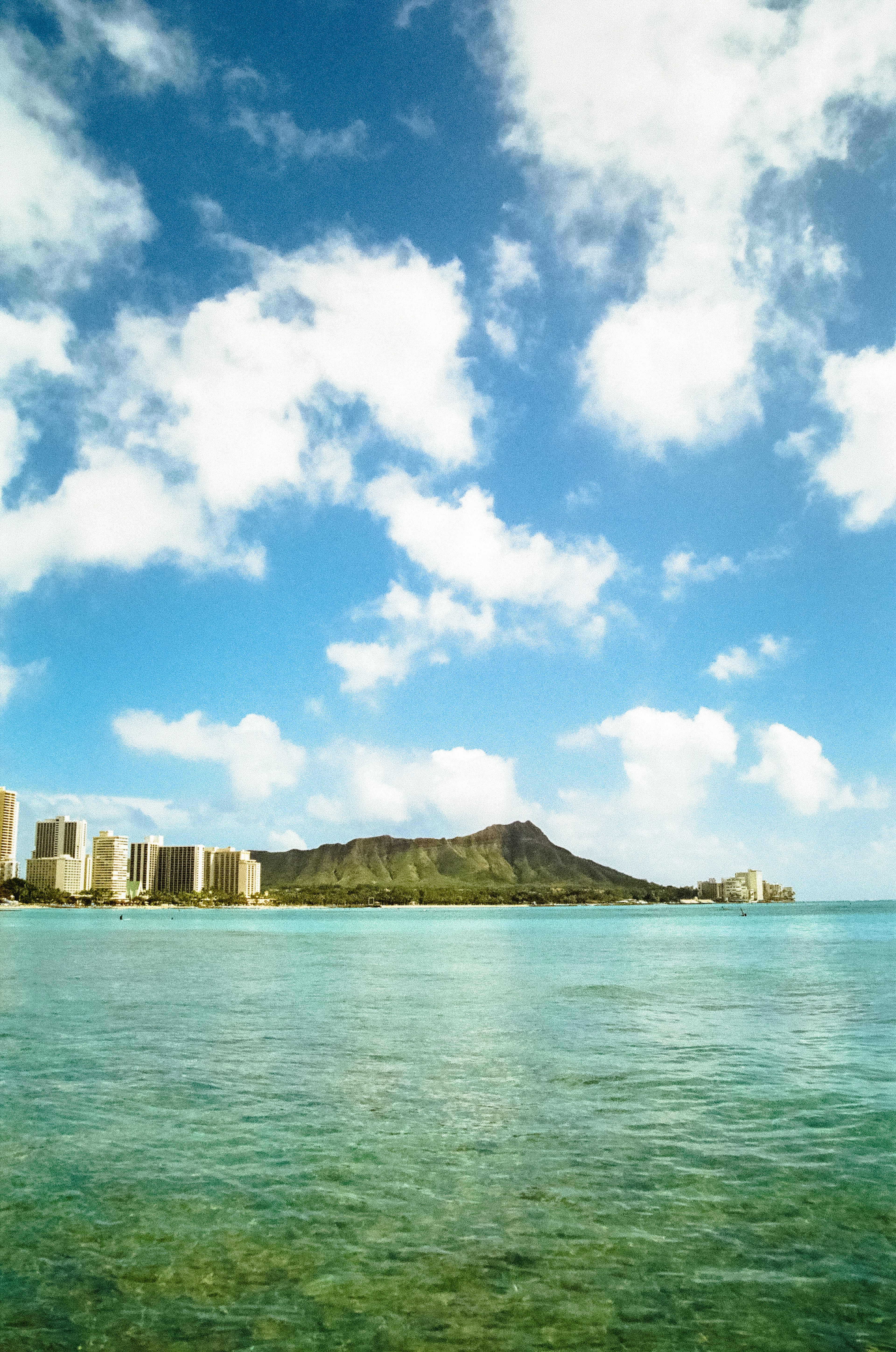 Pemandangan indah laut jernih dengan langit biru dan awan Gunung Diamond Head dan bangunan di latar belakang