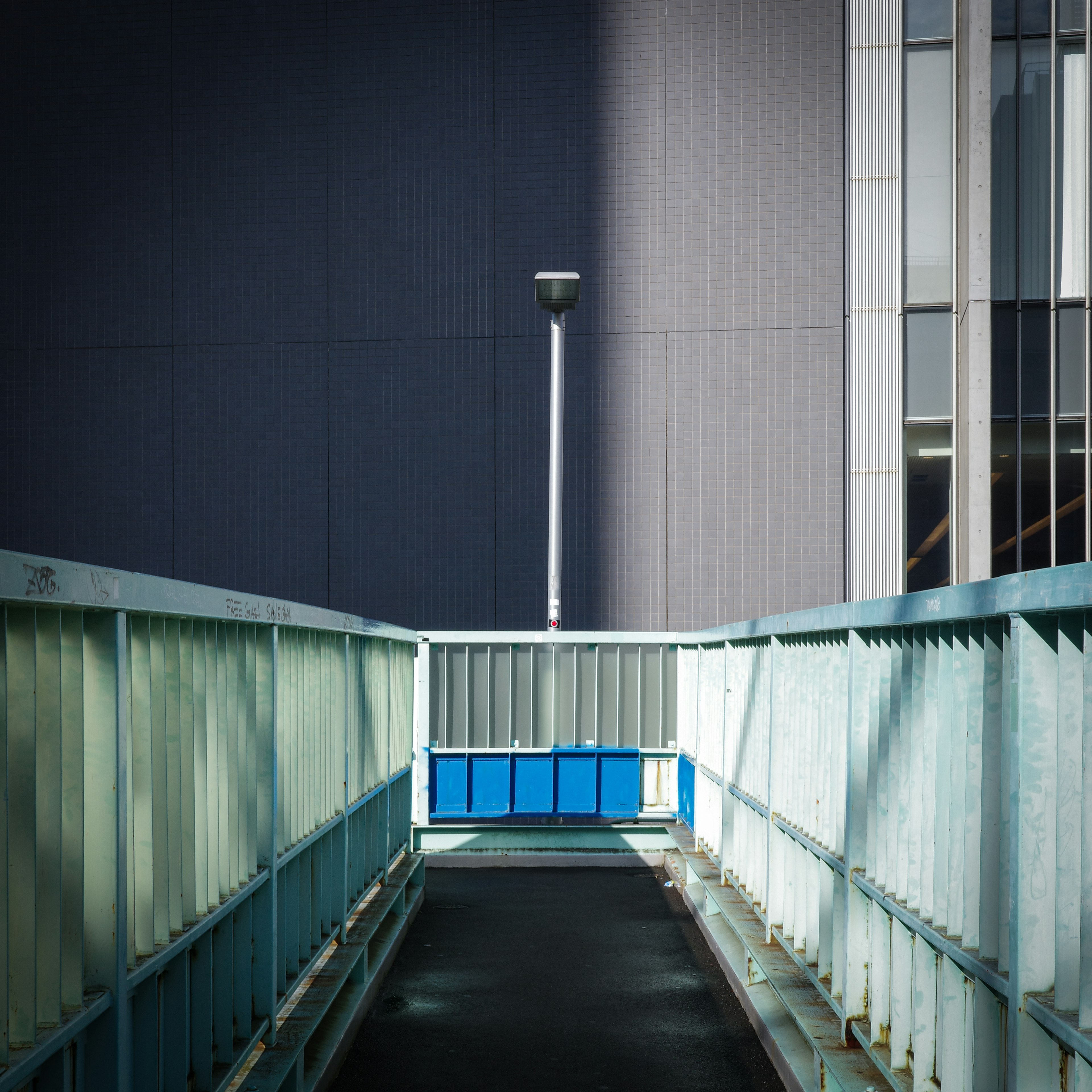 Una pasarela moderna con barandillas azules y una farola frente a un edificio