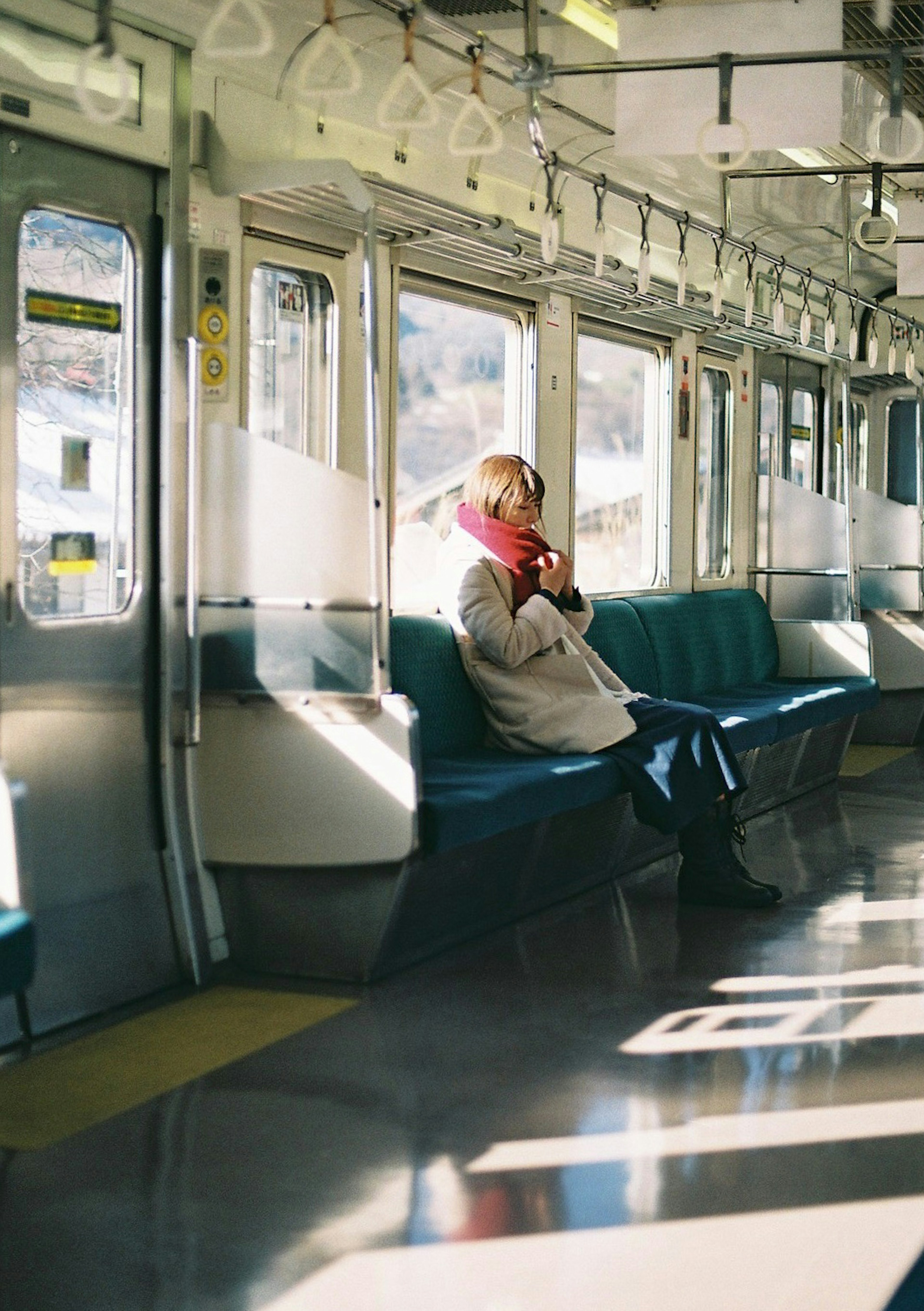 空の電車の車内で座っている女性　白いコートとピンクのスカーフ　自然光が差し込む