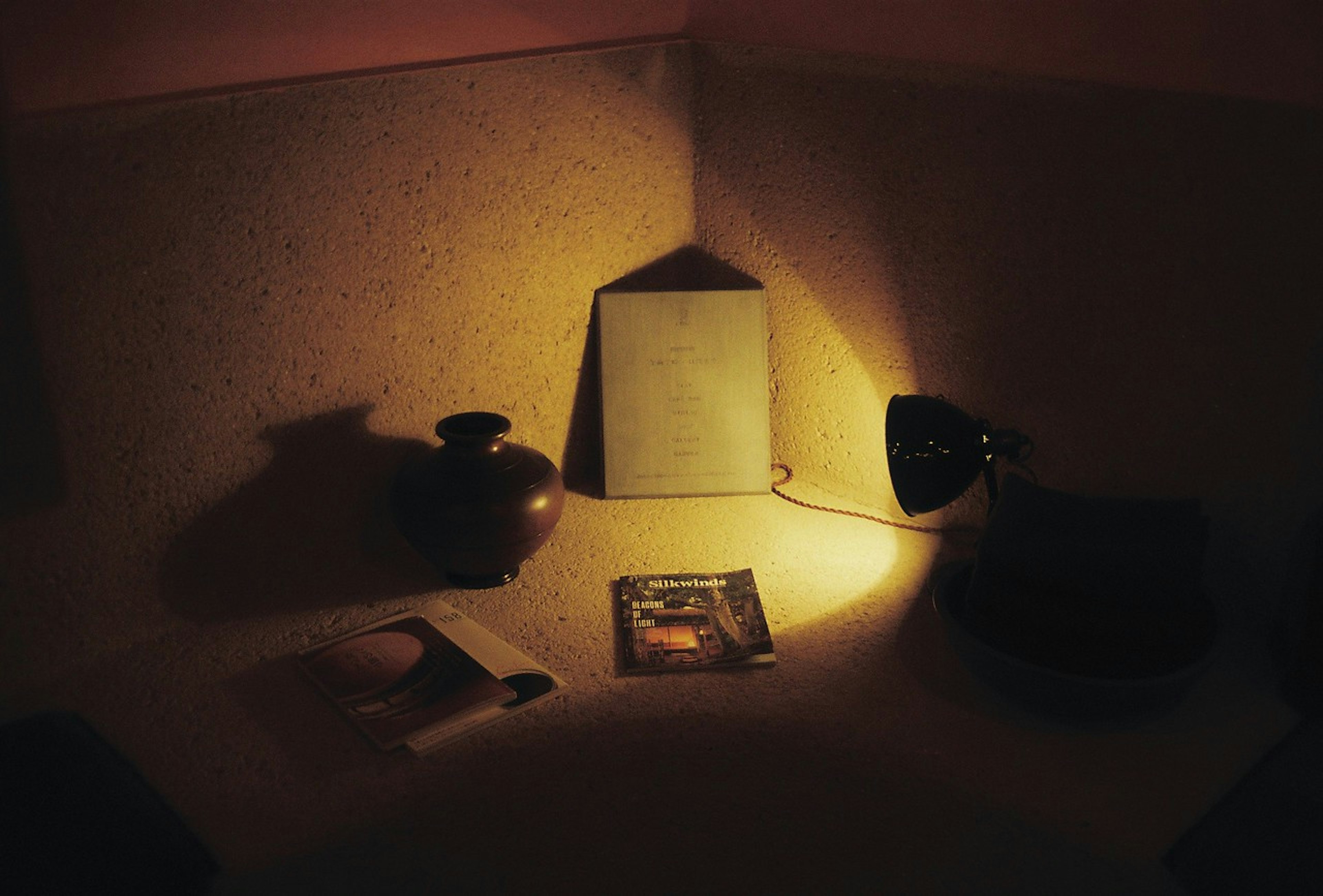 A simple still life with a ceramic vase and lamp in a dimly lit corner