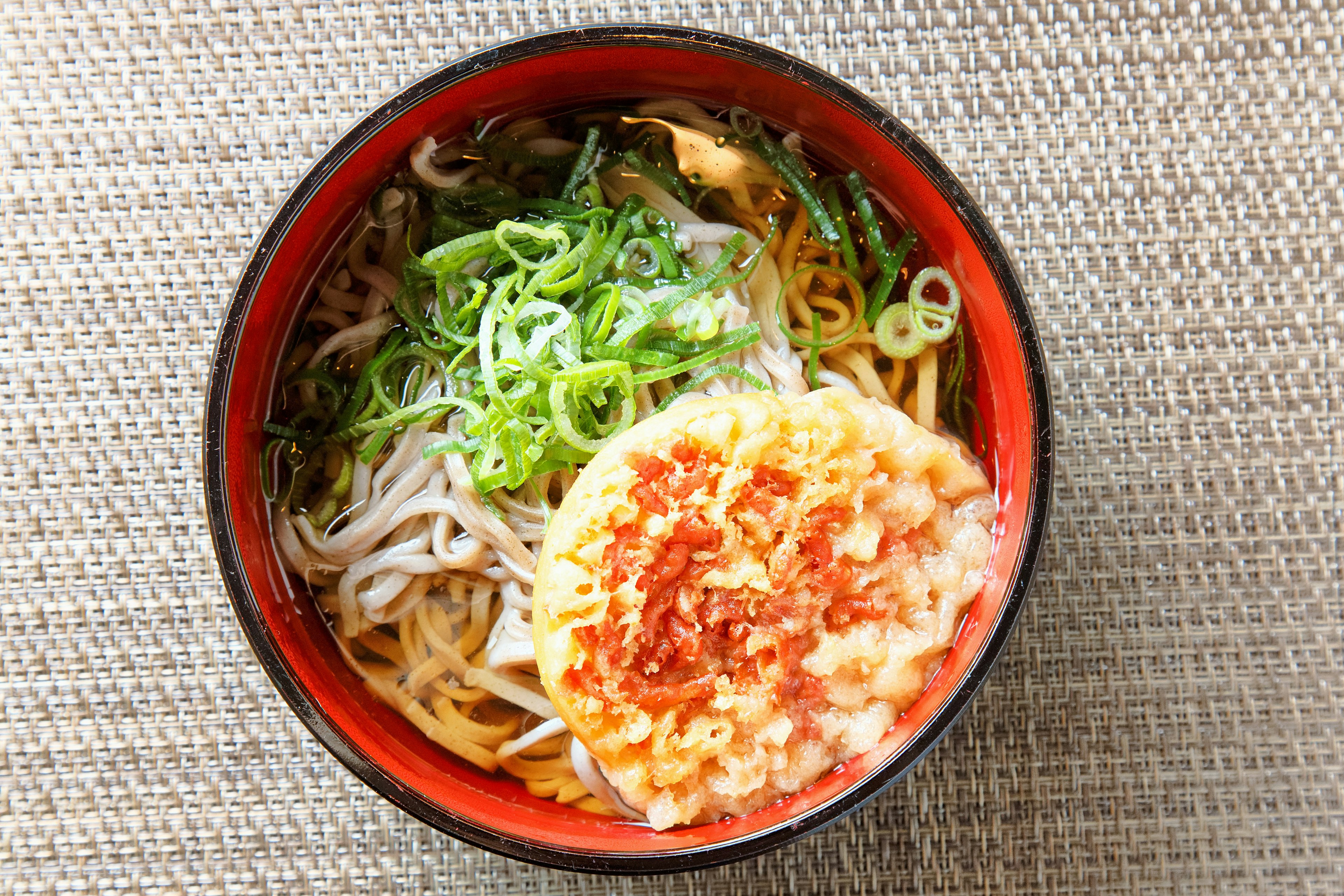 A bowl of ramen with green onions and a tempura topping