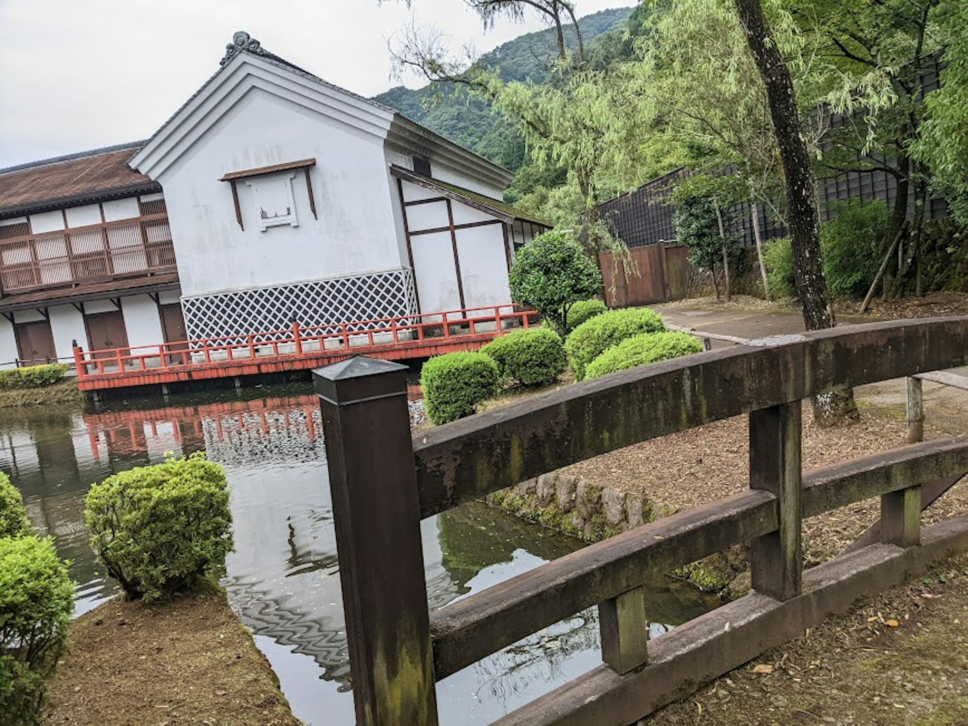 日本の伝統的な建物と池の風景、緑の植物と木製の橋が特徴