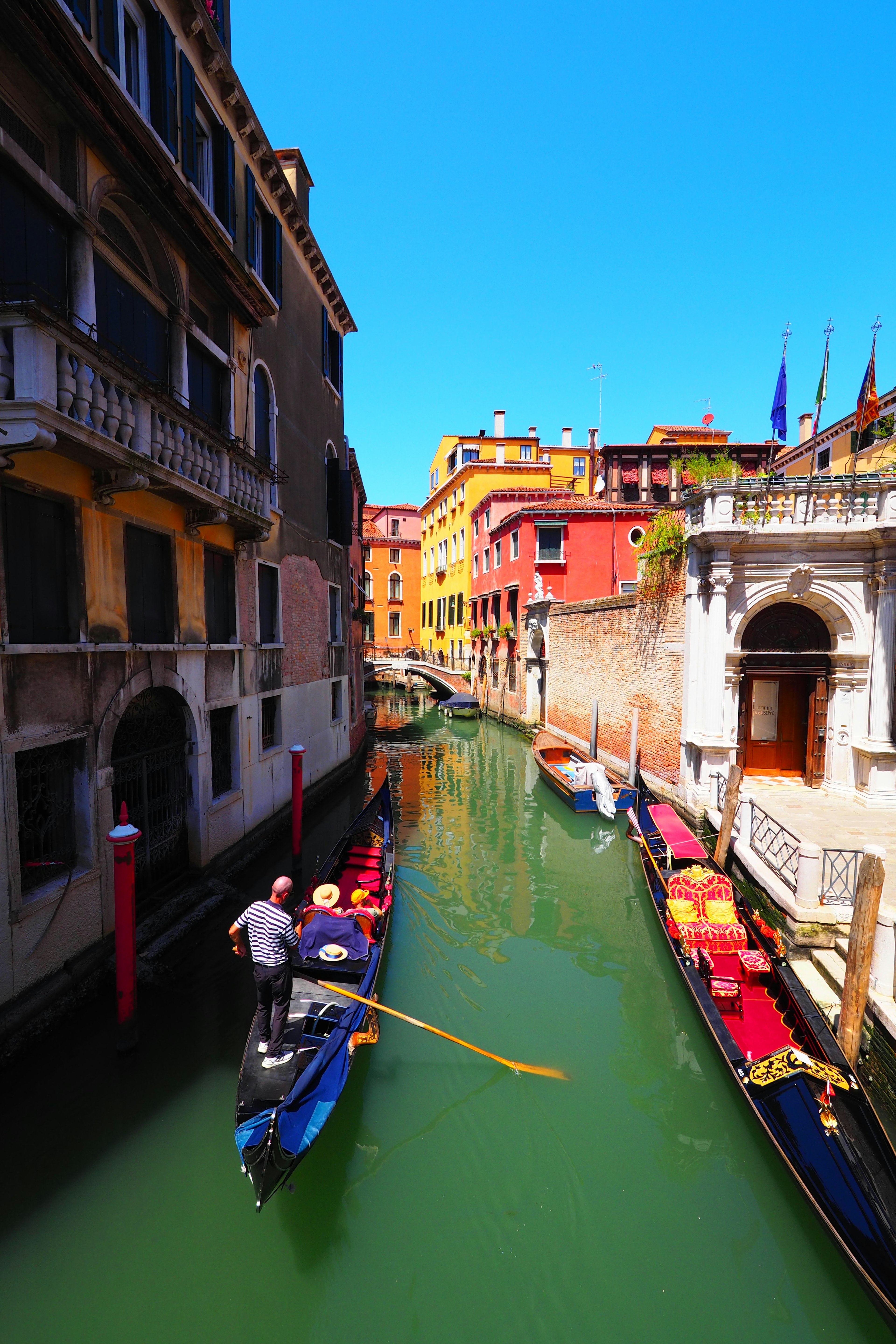 Người chèo gondola đang chèo thuyền trong kênh Venice xung quanh là những tòa nhà đầy màu sắc