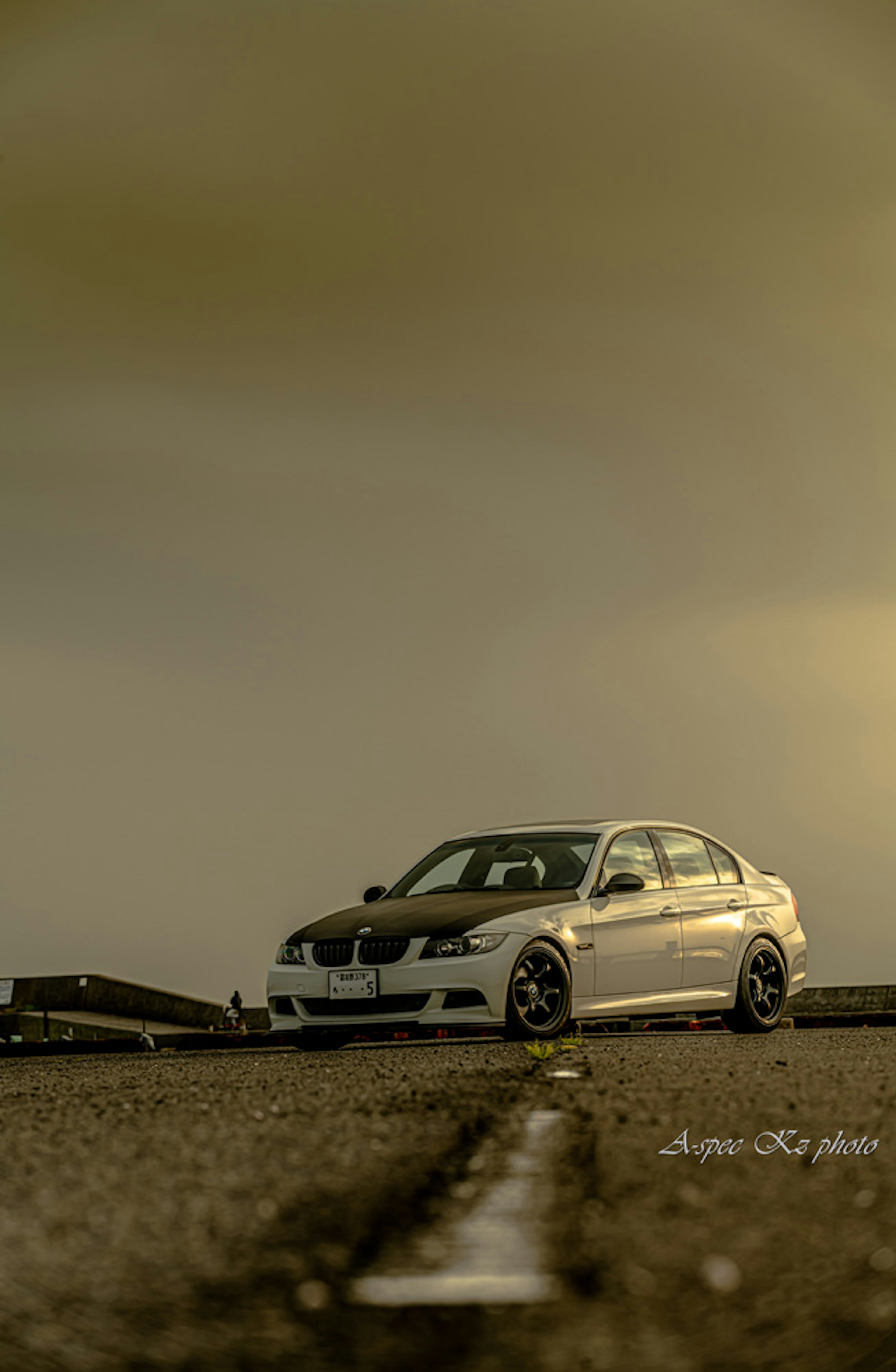 A white car parked on a wide road under cloudy skies