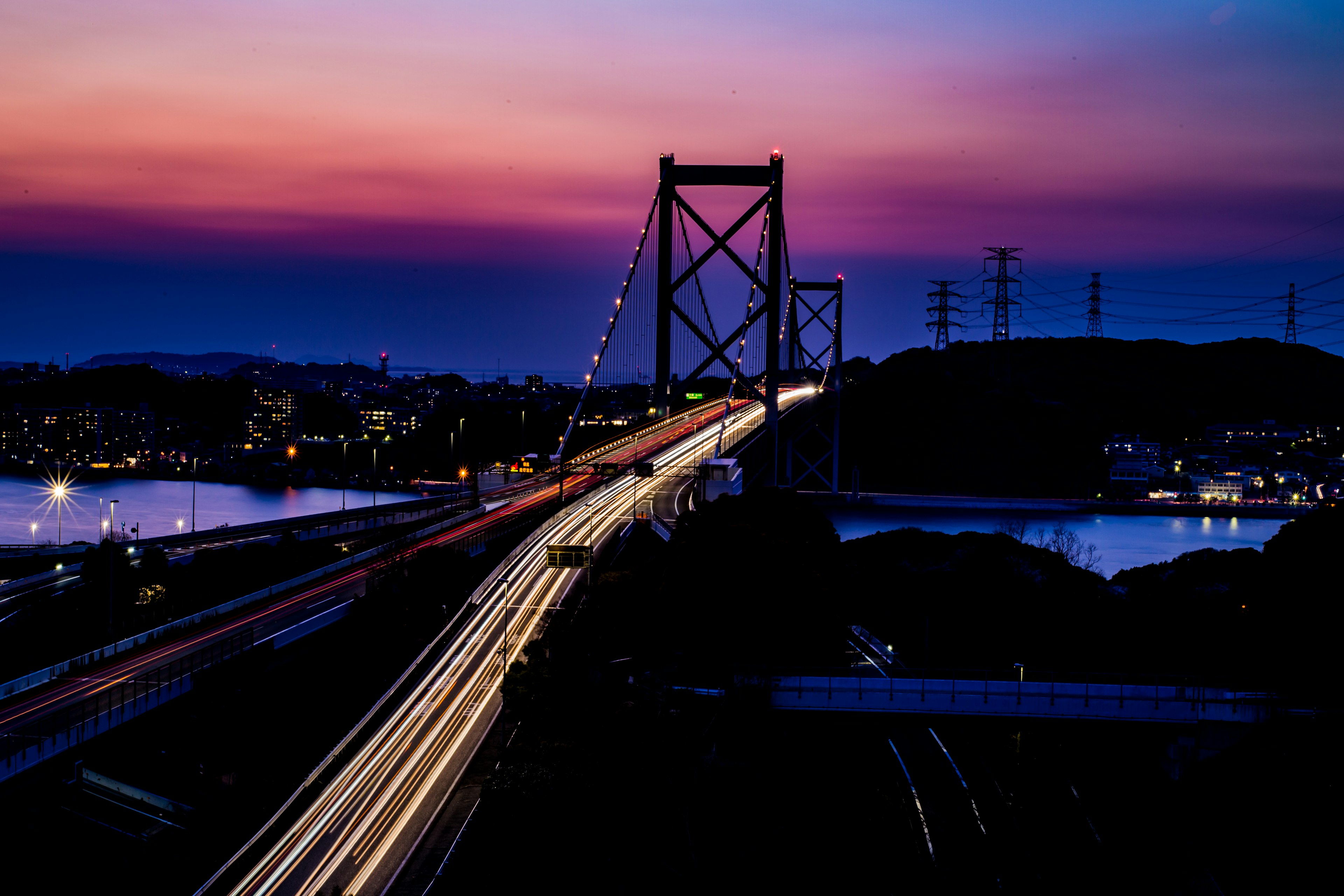 Pemandangan indah jembatan saat matahari terbenam dengan lampu mobil mengalir