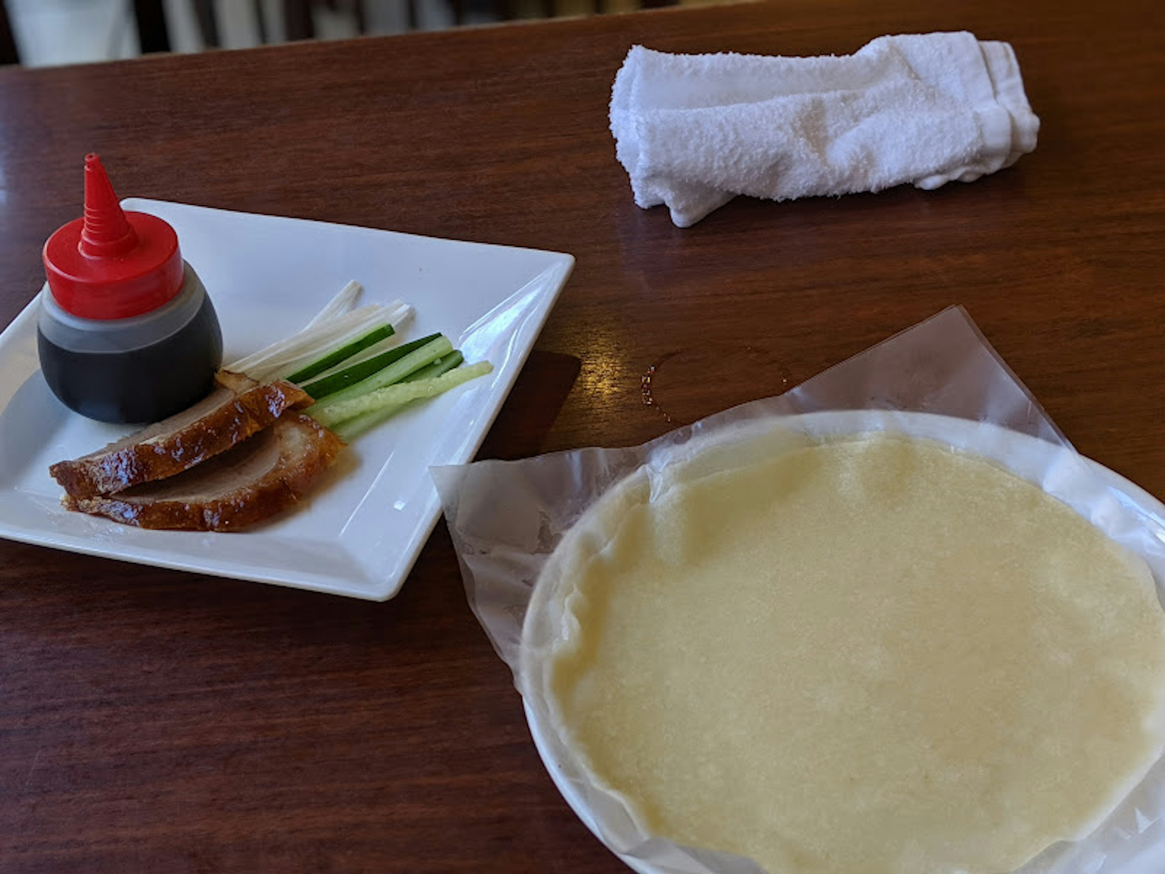 Sliced duck meat with green onions and sauce bottle on a plate with thin dough