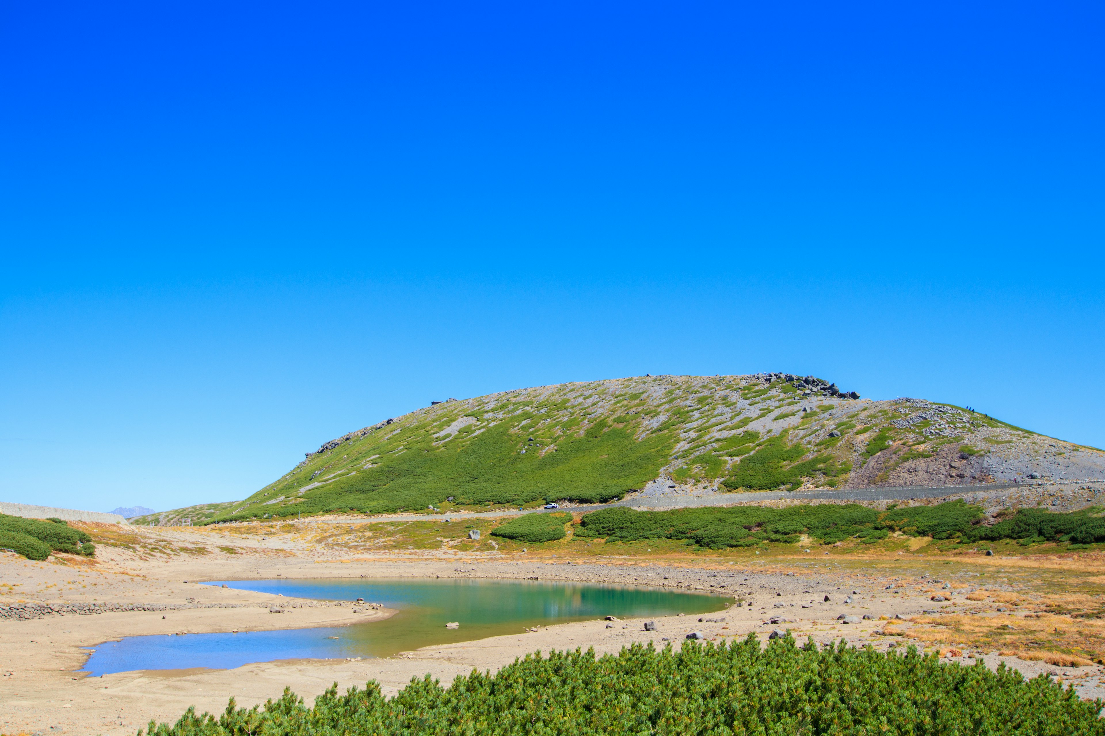 Landschaft mit klarem blauen Himmel und grünen Hügeln mit einem Gewässer