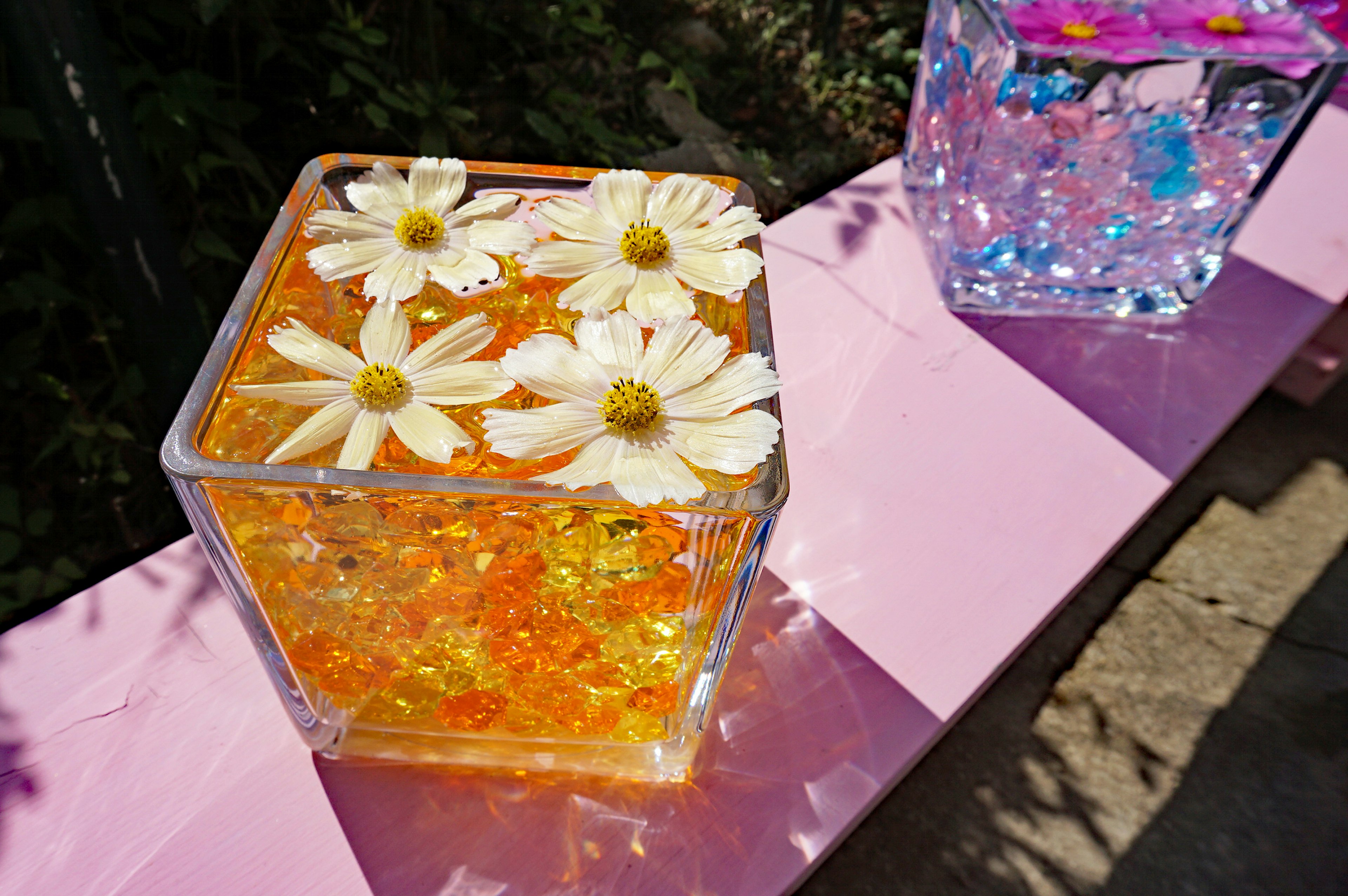 Klarer quadratischer Behälter mit weißen Blumen, die in orangefarbenem Gel schwimmen