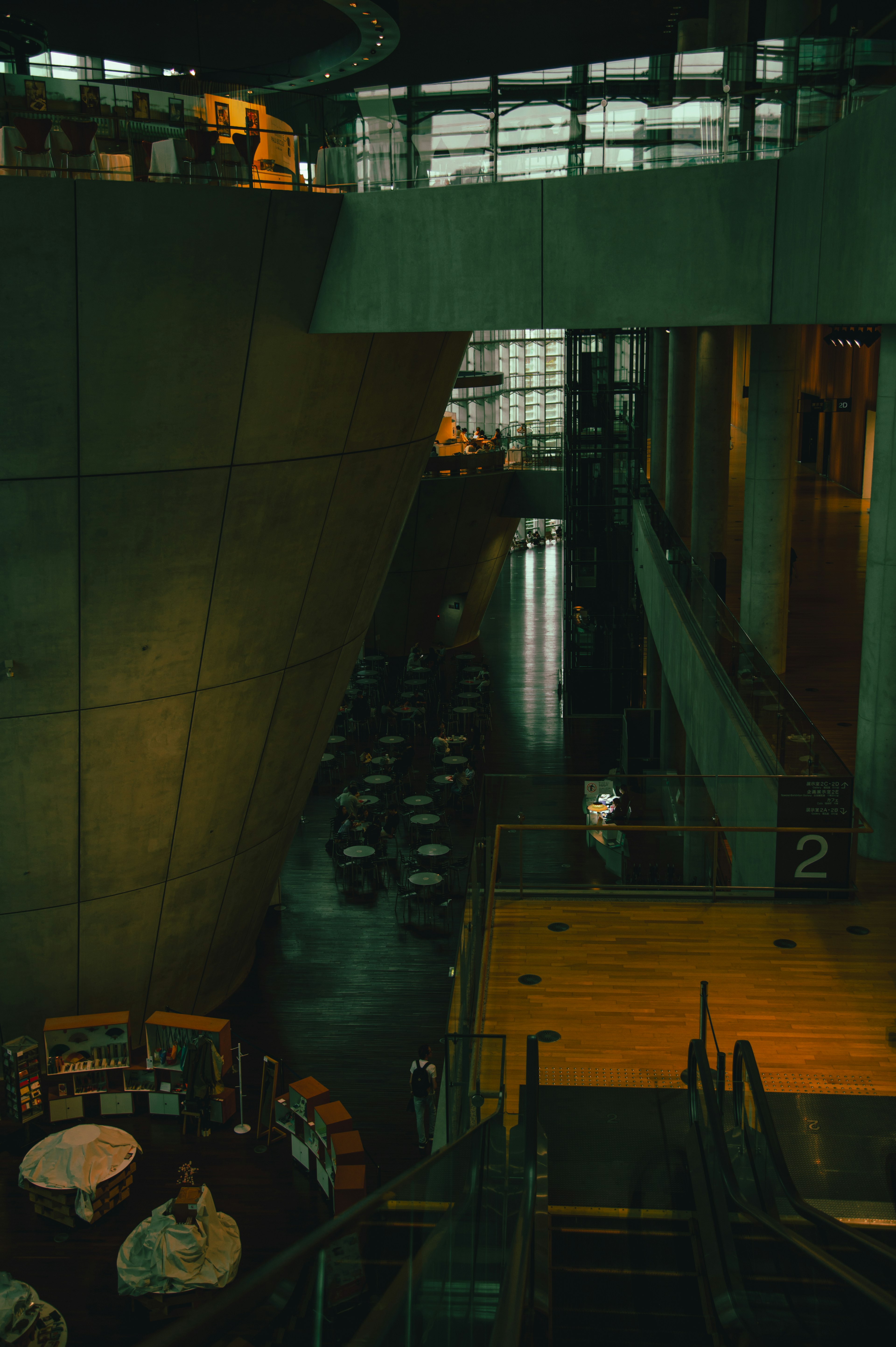 Innenraum eines modernen Gebäudes mit Rolltreppe und Essbereich in dunklen Tönen