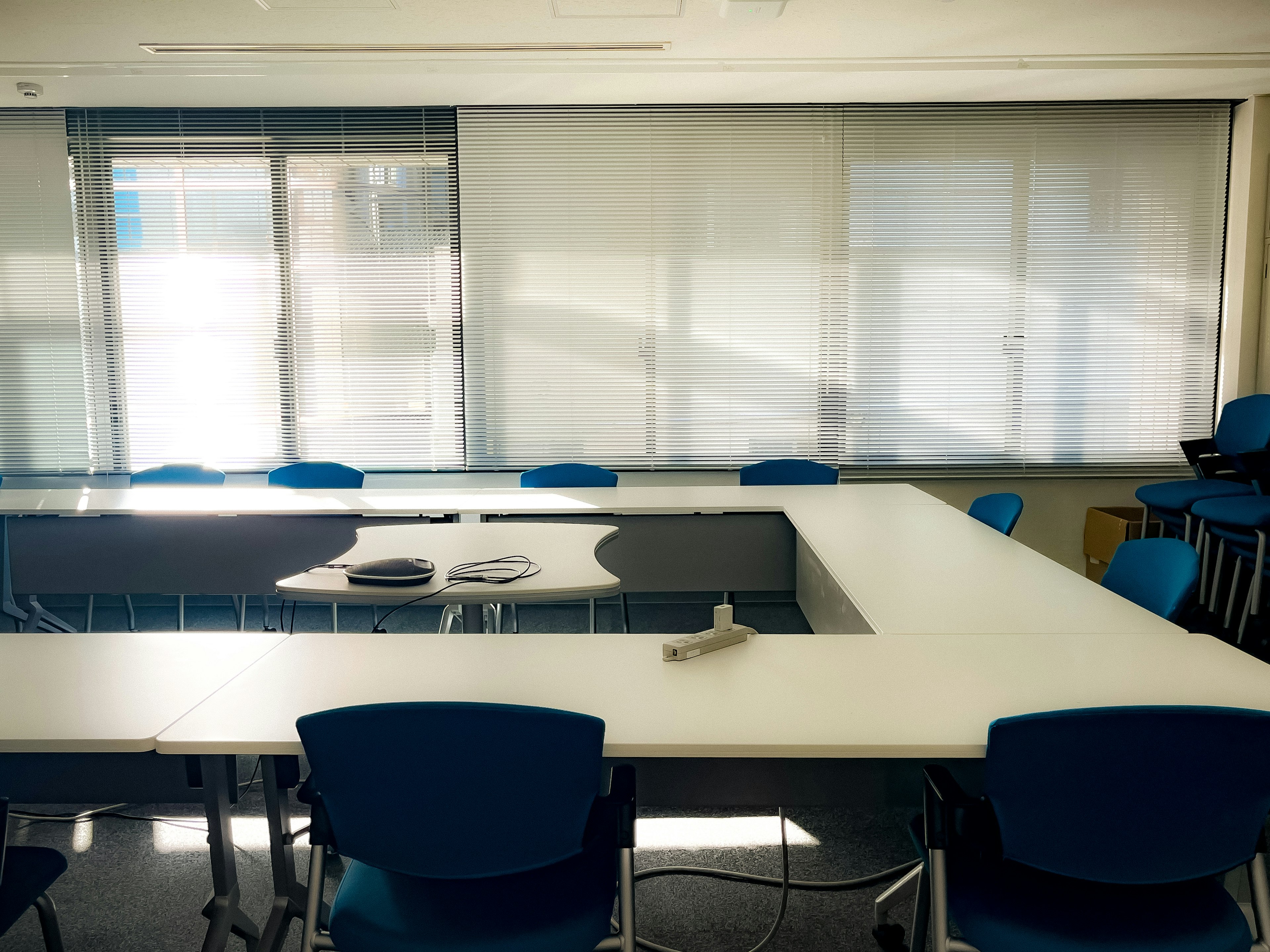 Ruang rapat kantor yang terang dengan meja putih dan kursi biru tersusun