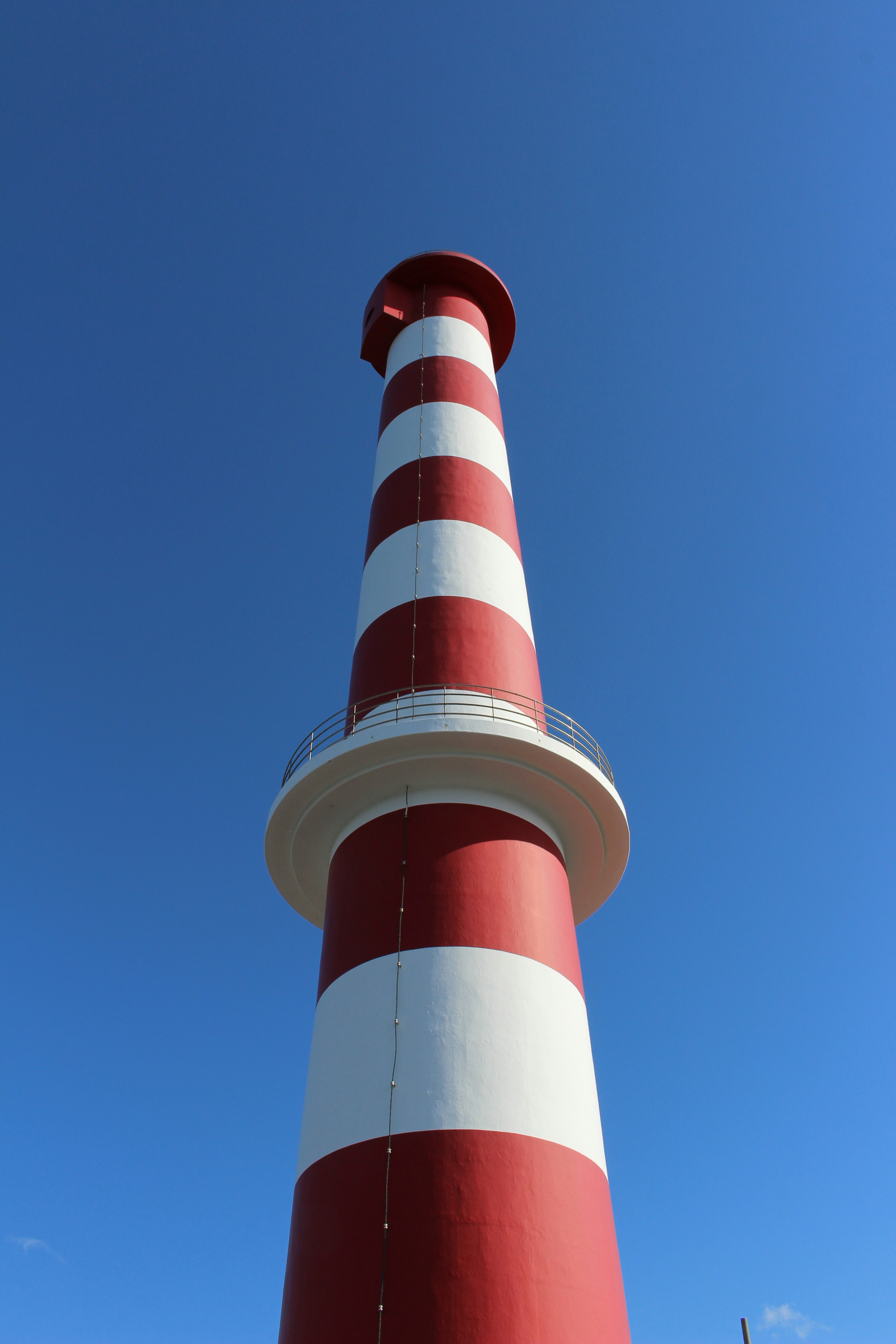 Ein rot-weiß gestreifter Leuchtturm steht unter einem blauen Himmel