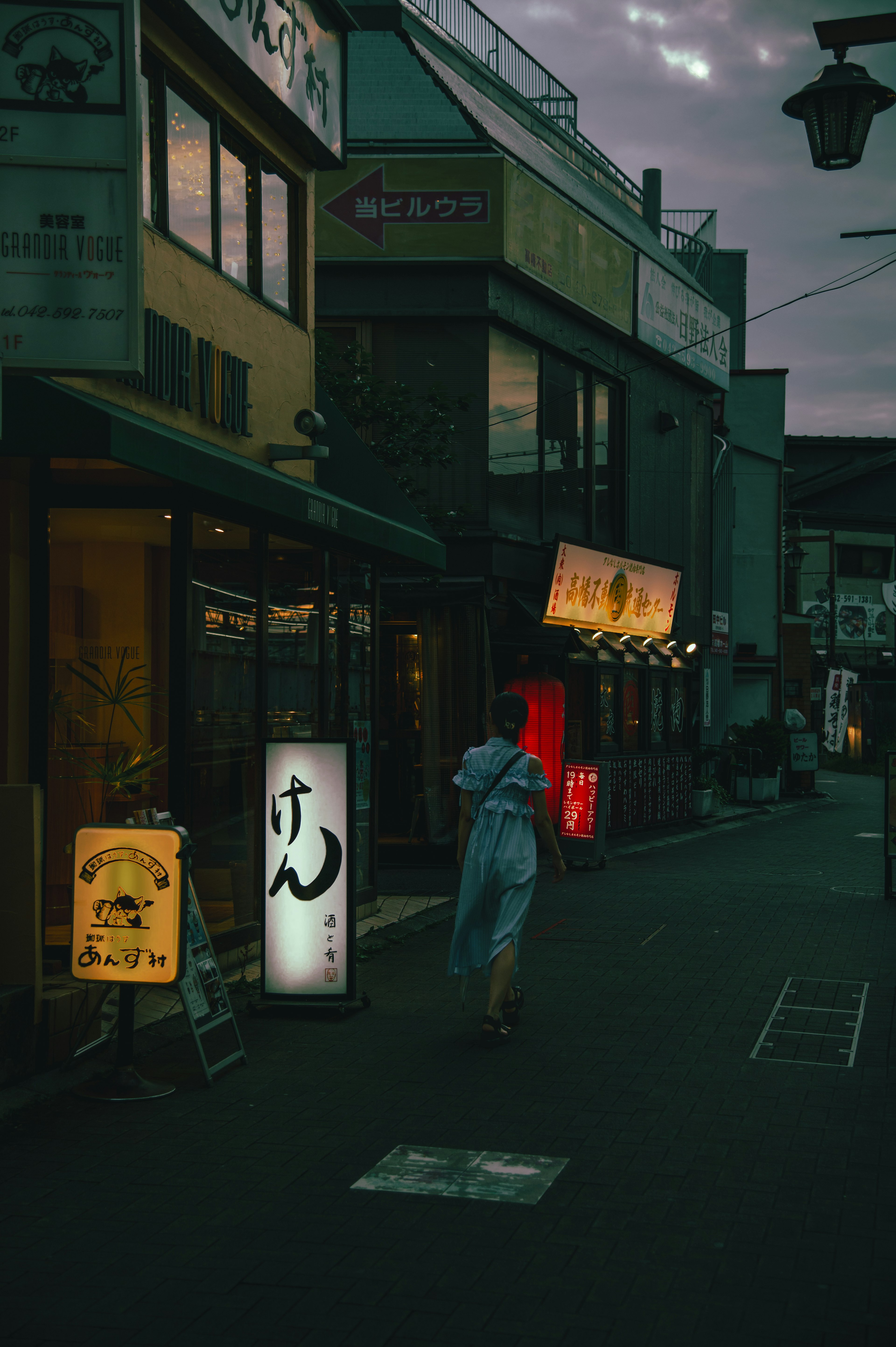 A person standing at a dimly lit street corner with restaurant signs