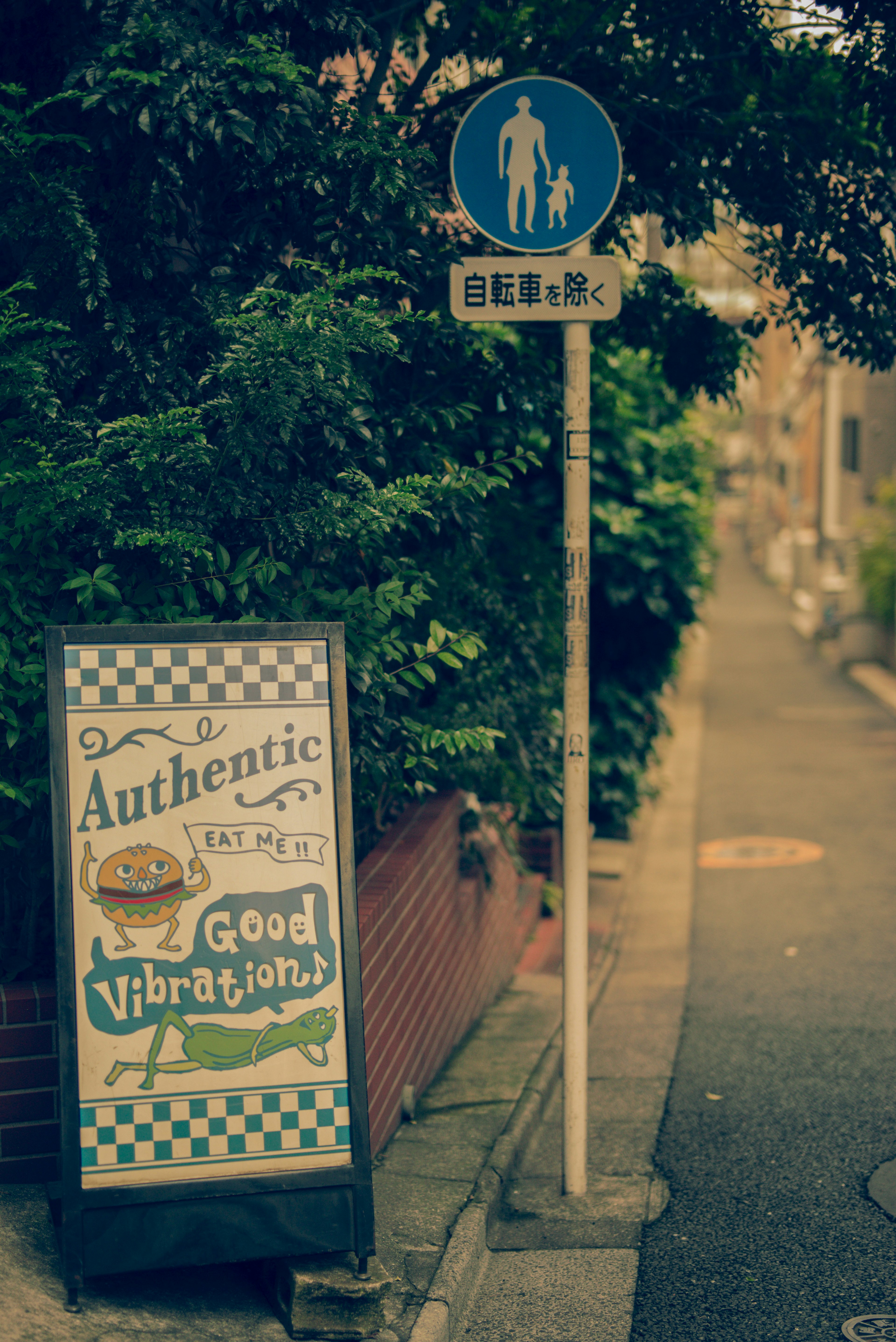 青い看板と道の標識がある狭い通りに立つ飲食店の看板