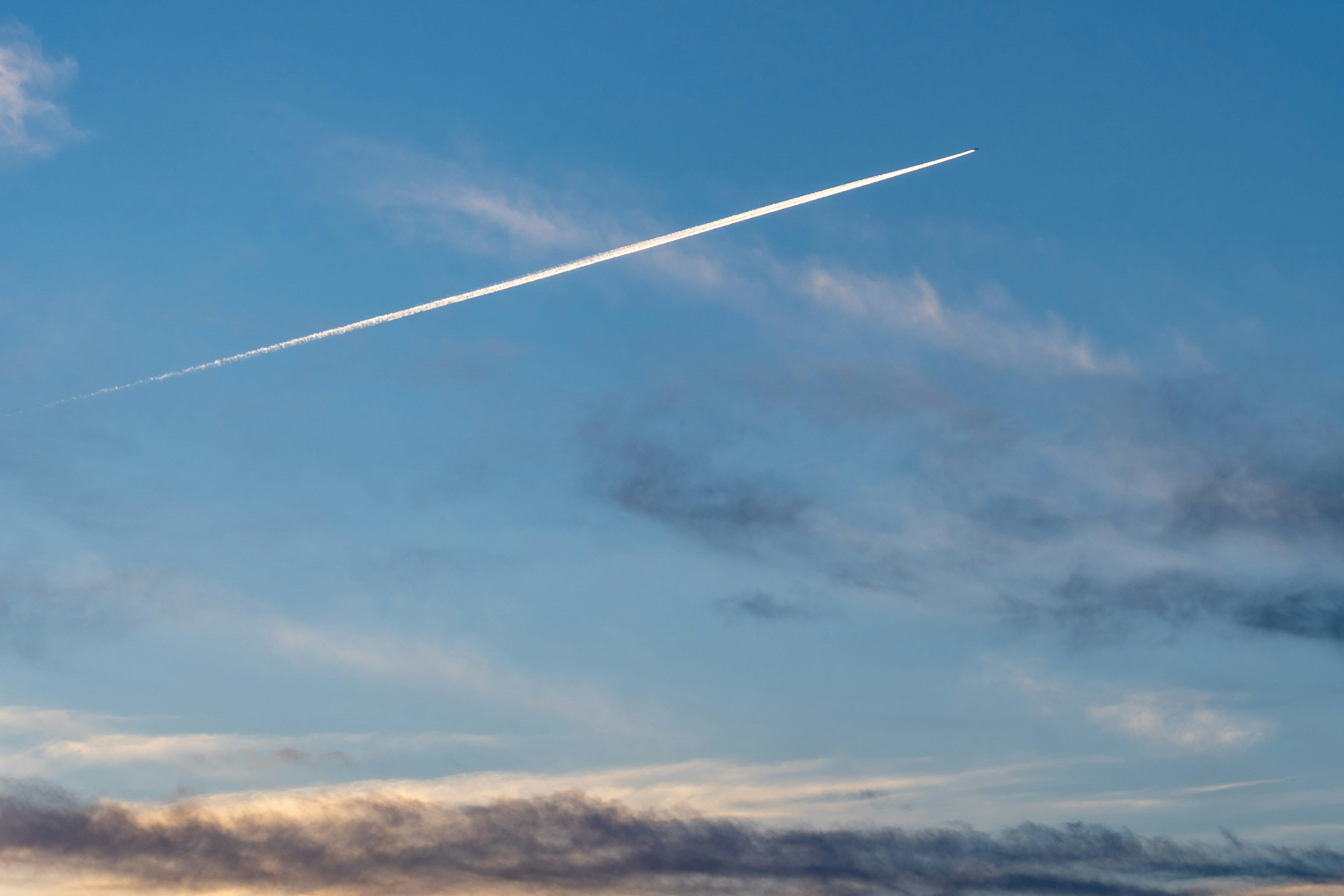 A contrail in a blue sky with wispy clouds