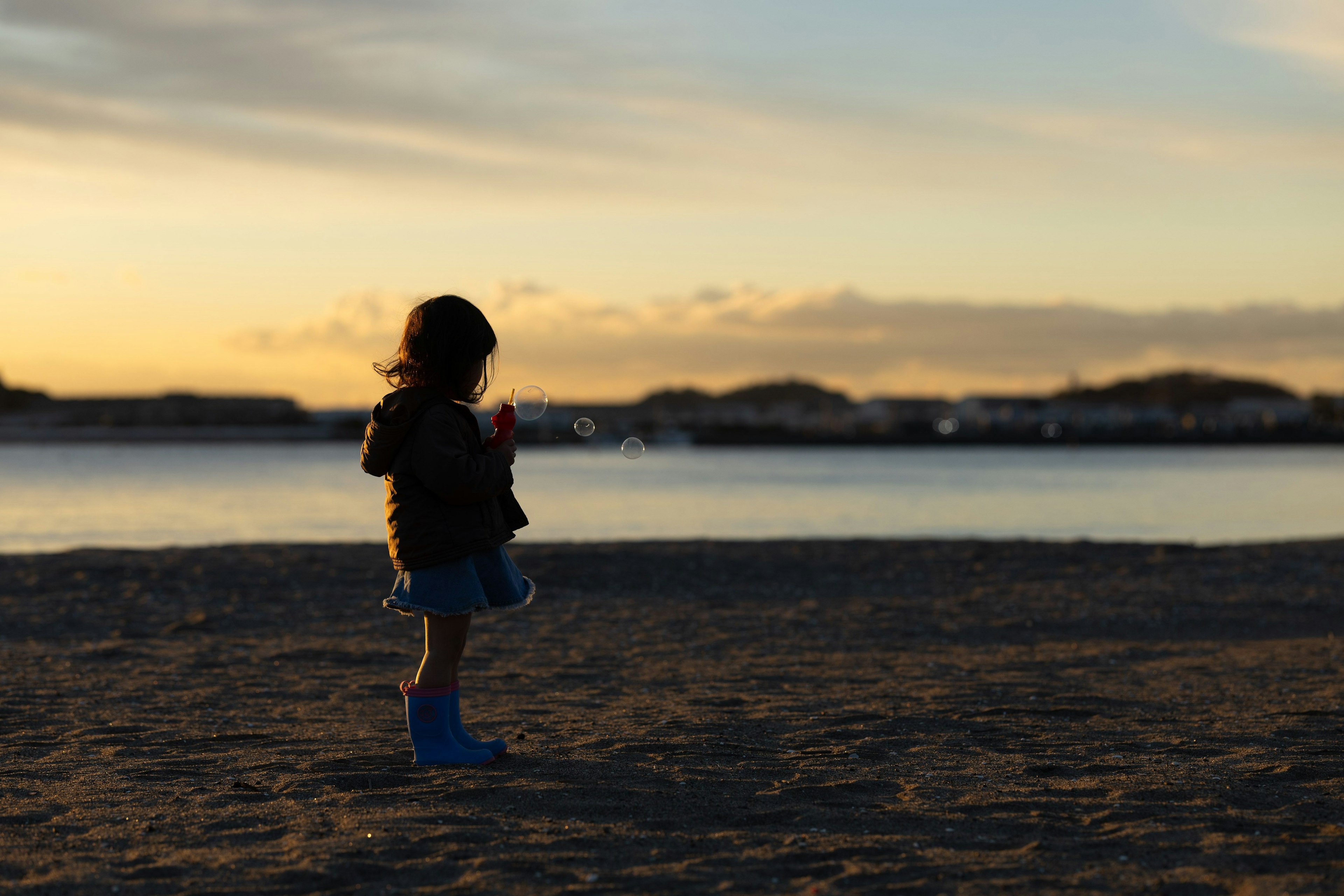 夕日を背にした子供が砂浜に立っている